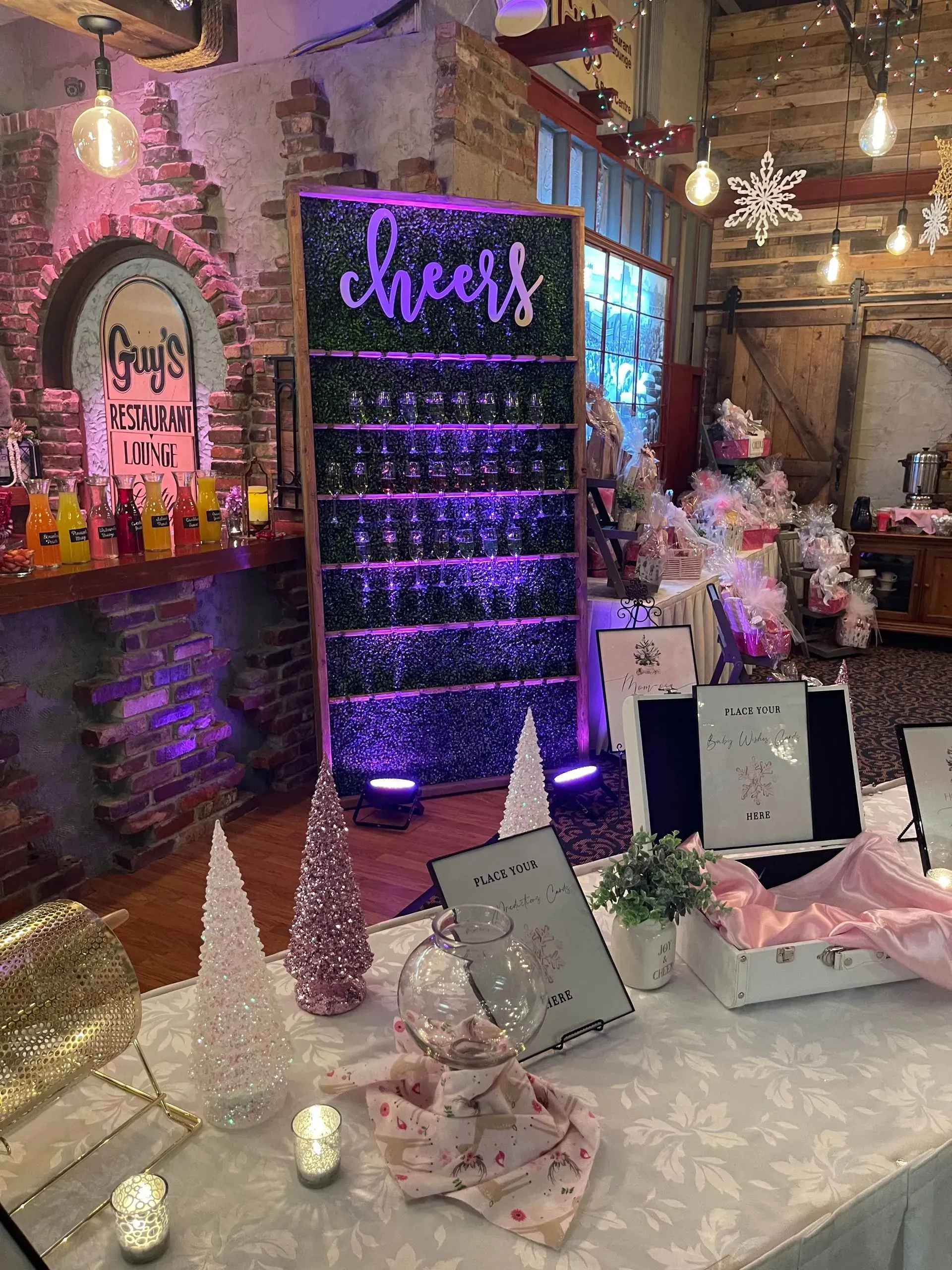 Decorated party dessert table with pink lights, purple champagne tower, and glittery decor in a rustic room
