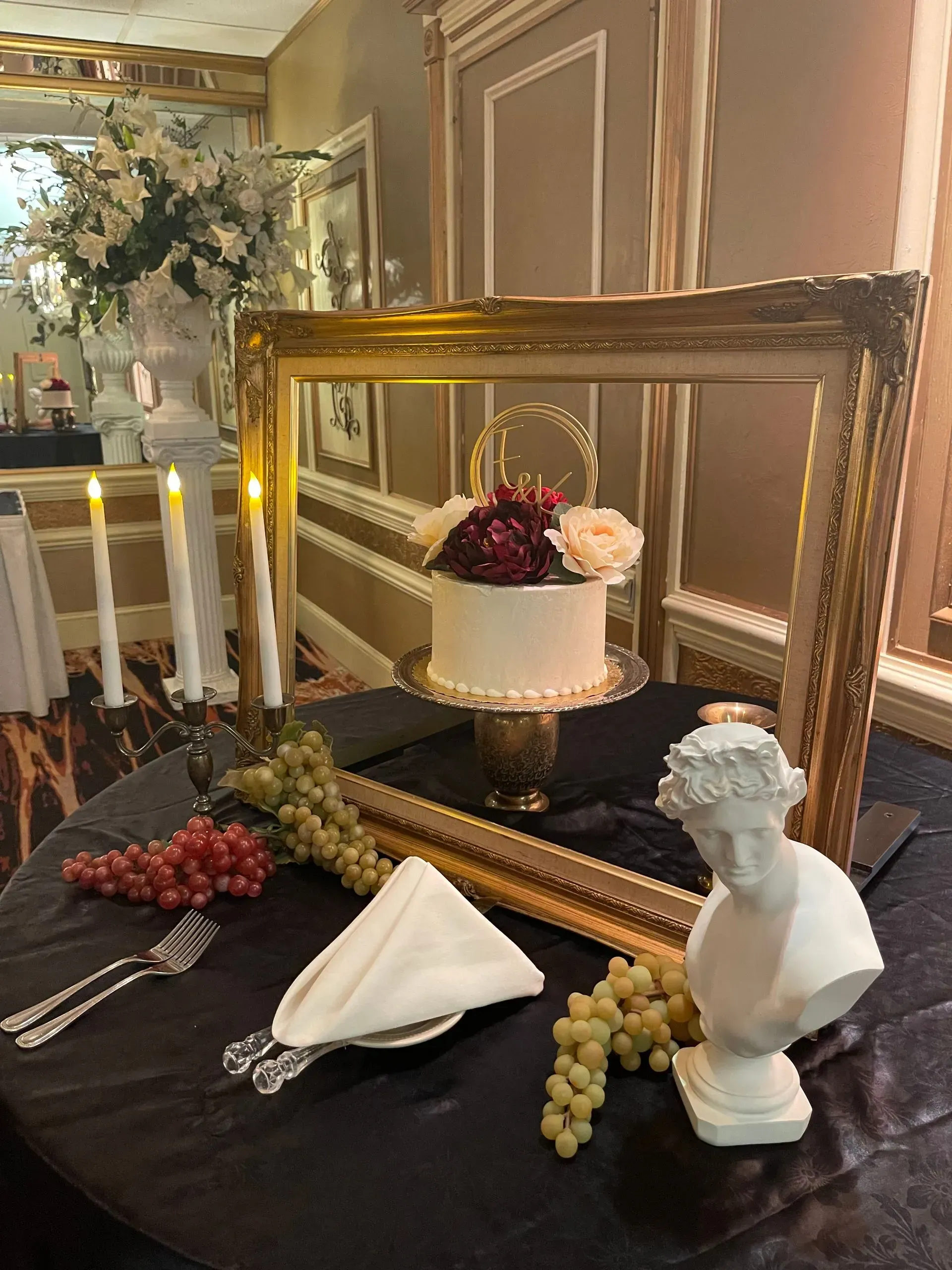 Decorated dining table with cake, grapes, candles, folded napkin, and framed mirror in a formal room