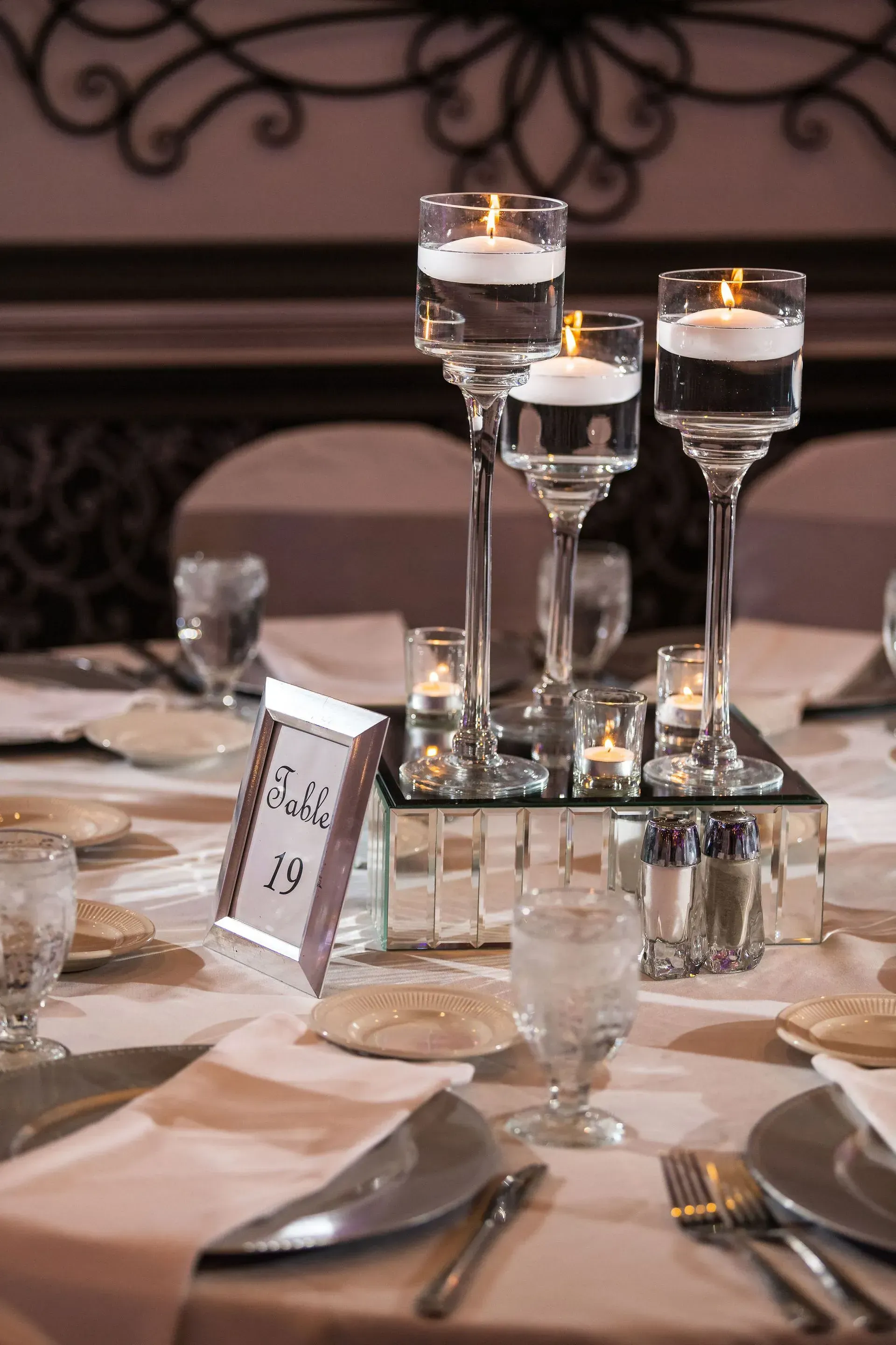 Elegant banquet table with mirrored candle holders, votives, plates, and silverware on a formal dining setting