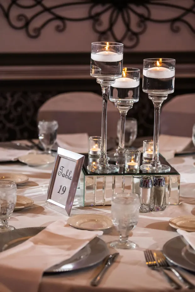 Elegant banquet table centerpiece with floating candles, glass holders, and a mirrored base.