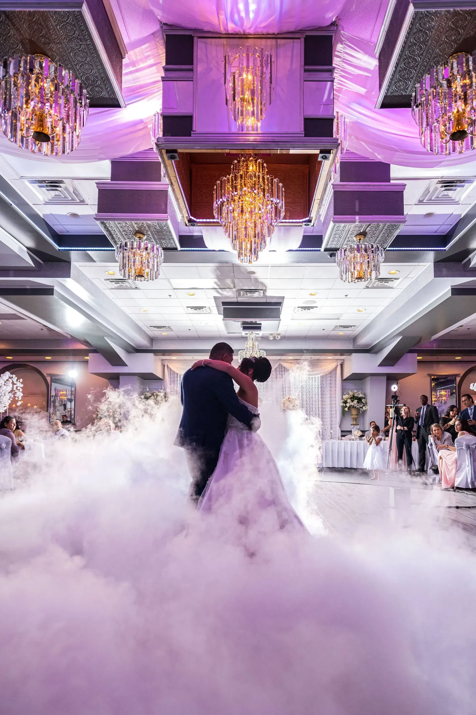 Couple dancing in a purple-lit ballroom with low-lying fog and chandeliers