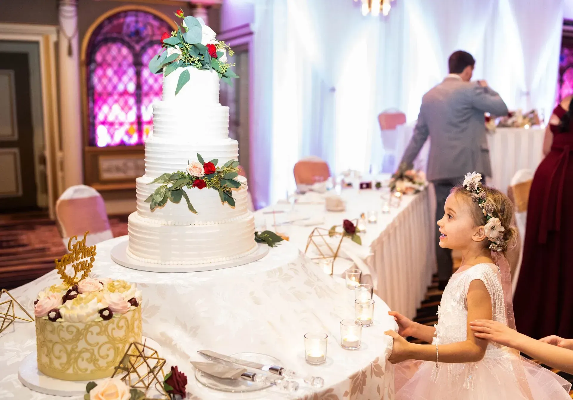 Girl in a pink dress standing by a decorated wedding cake at a reception table