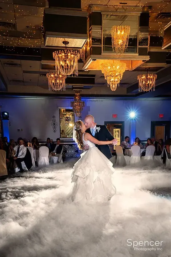 Bride and groom dancing in a cloud of fog beneath chandeliers at a wedding reception