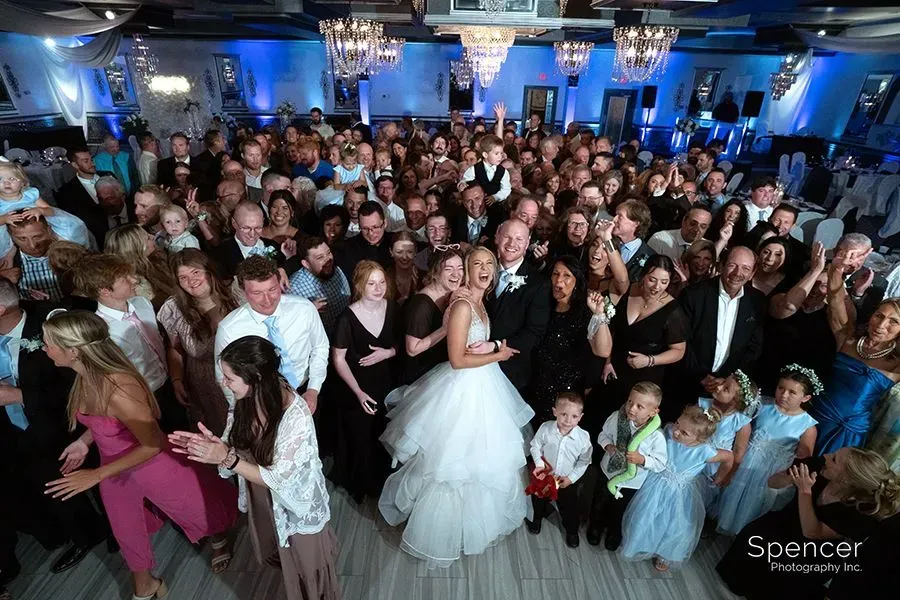 Crowded wedding reception with a bride in a white gown and guests gathered on the dance floor