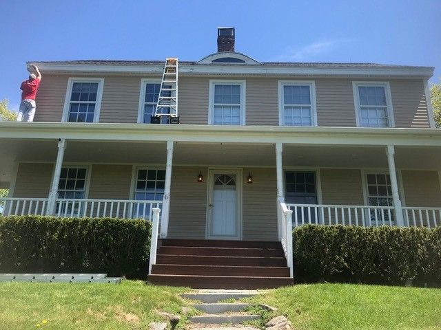 A man is painting the roof of a house with a ladder.