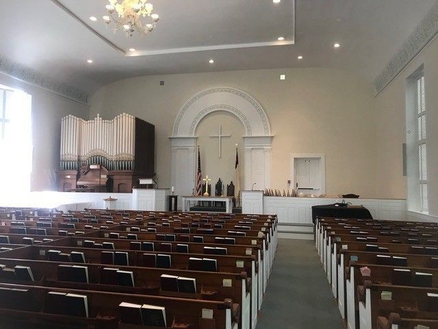 The inside of a church with rows of wooden benches and a chandelier hanging from the ceiling.