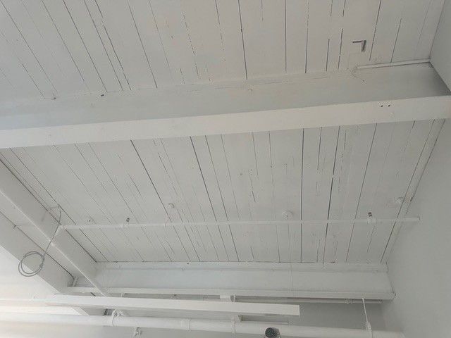 A white ceiling with wooden beams and pipes in a room.
