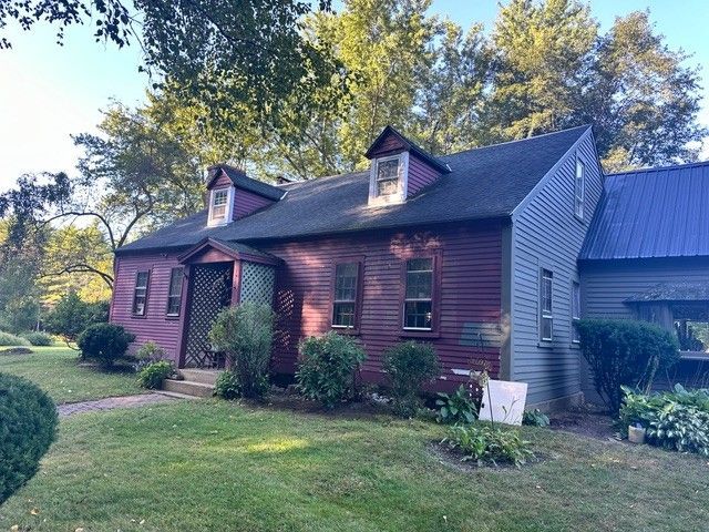 A red house with a black roof is surrounded by trees and grass.