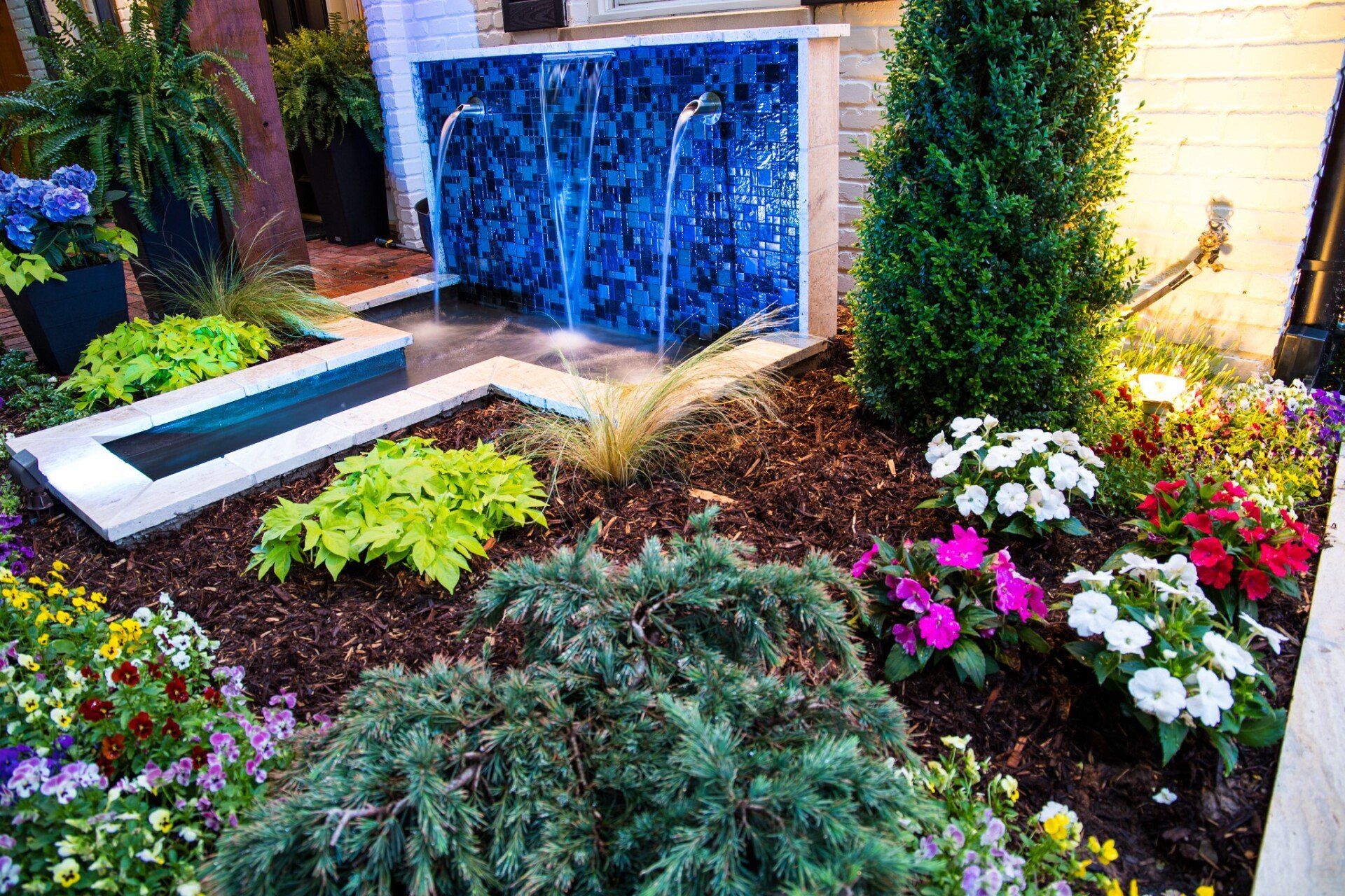 There is a waterfall in the middle of the garden surrounded by flowers.