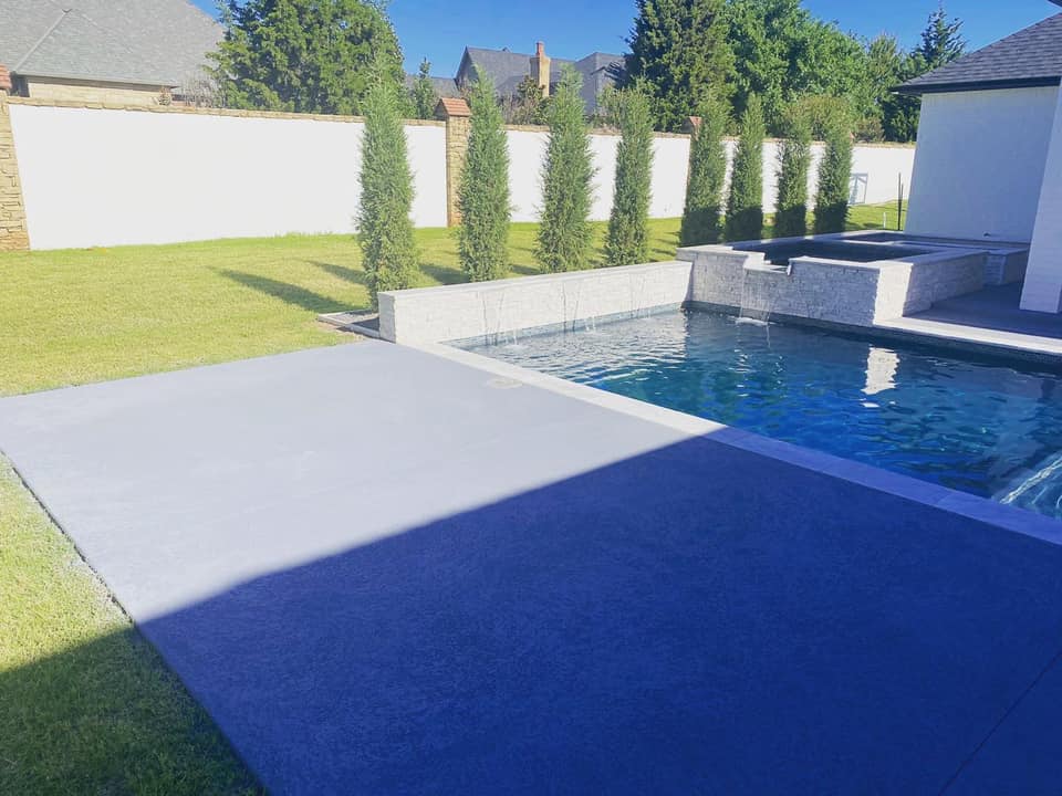 A large swimming pool is surrounded by a lush green lawn and trees.