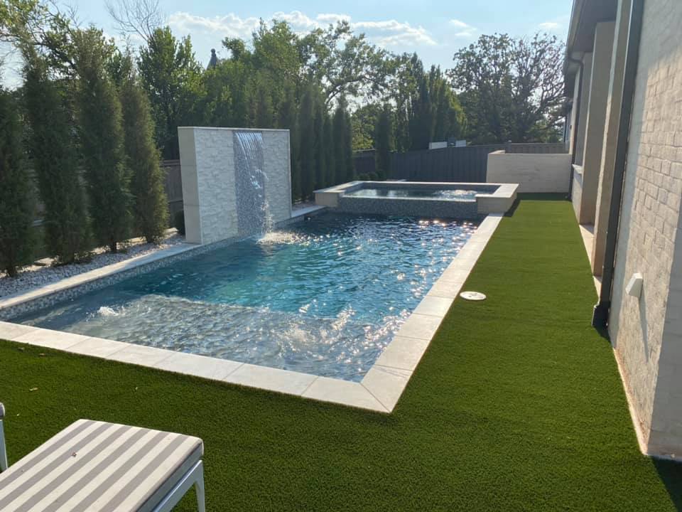 A large swimming pool with a waterfall in the backyard of a house.