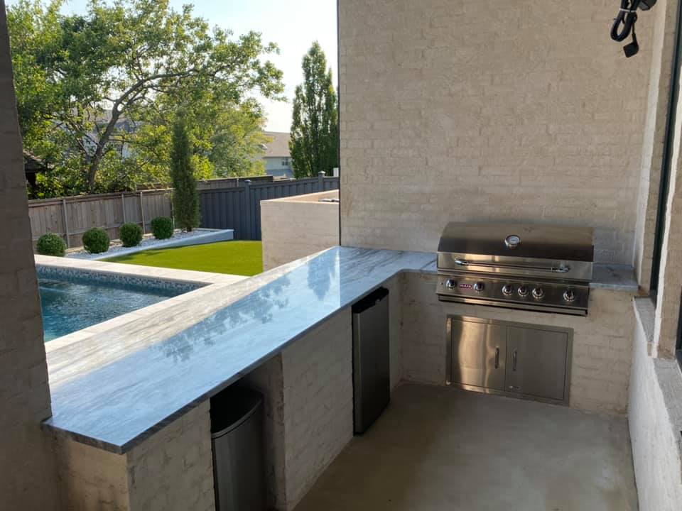 A patio with a grill and a swimming pool in the background.
