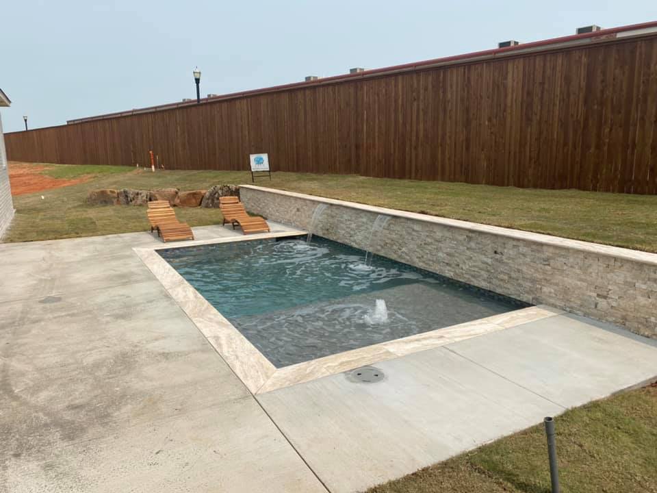 There is a swimming pool in the backyard with a wooden fence in the background.