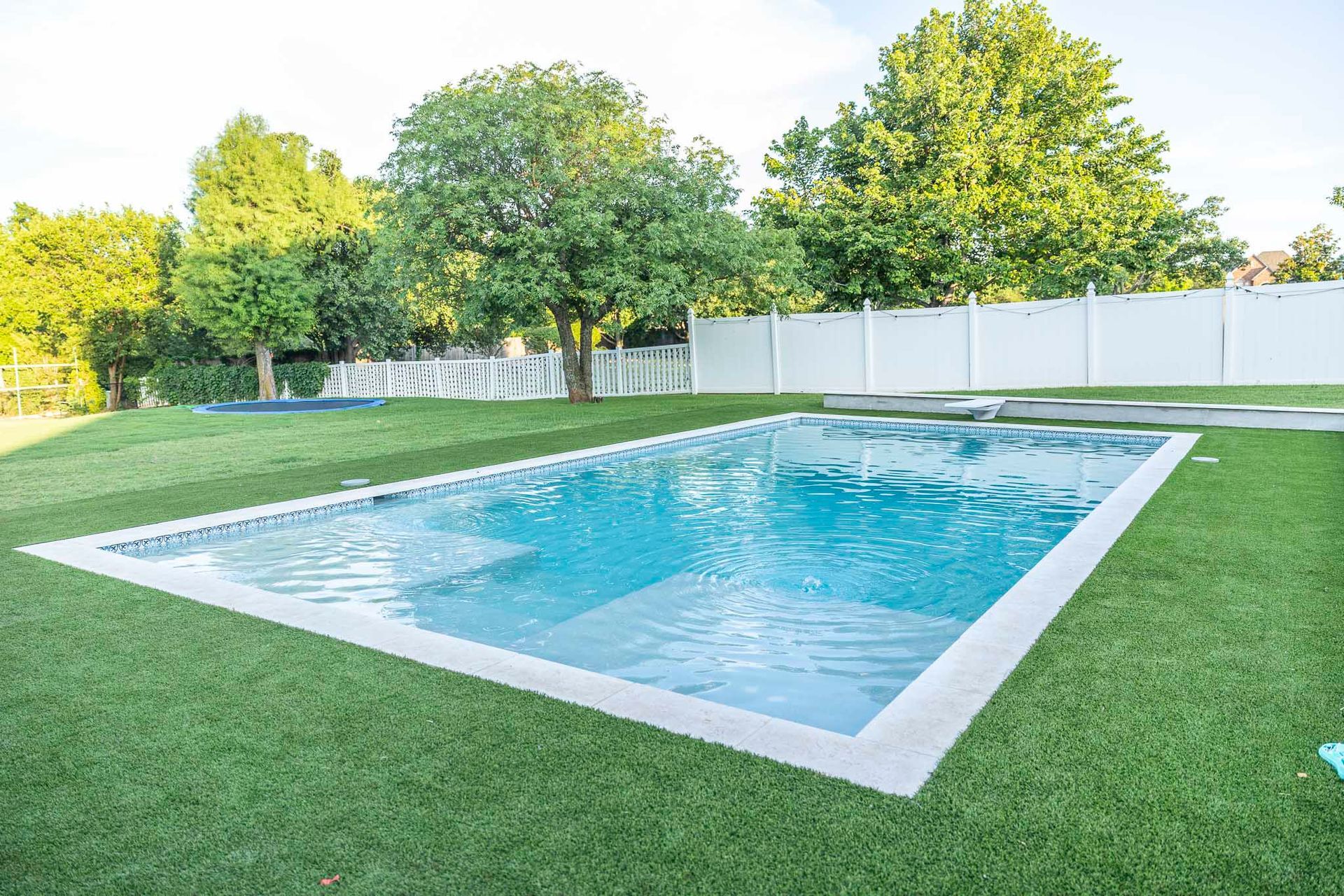 A large swimming pool surrounded by grass and trees in a backyard.
