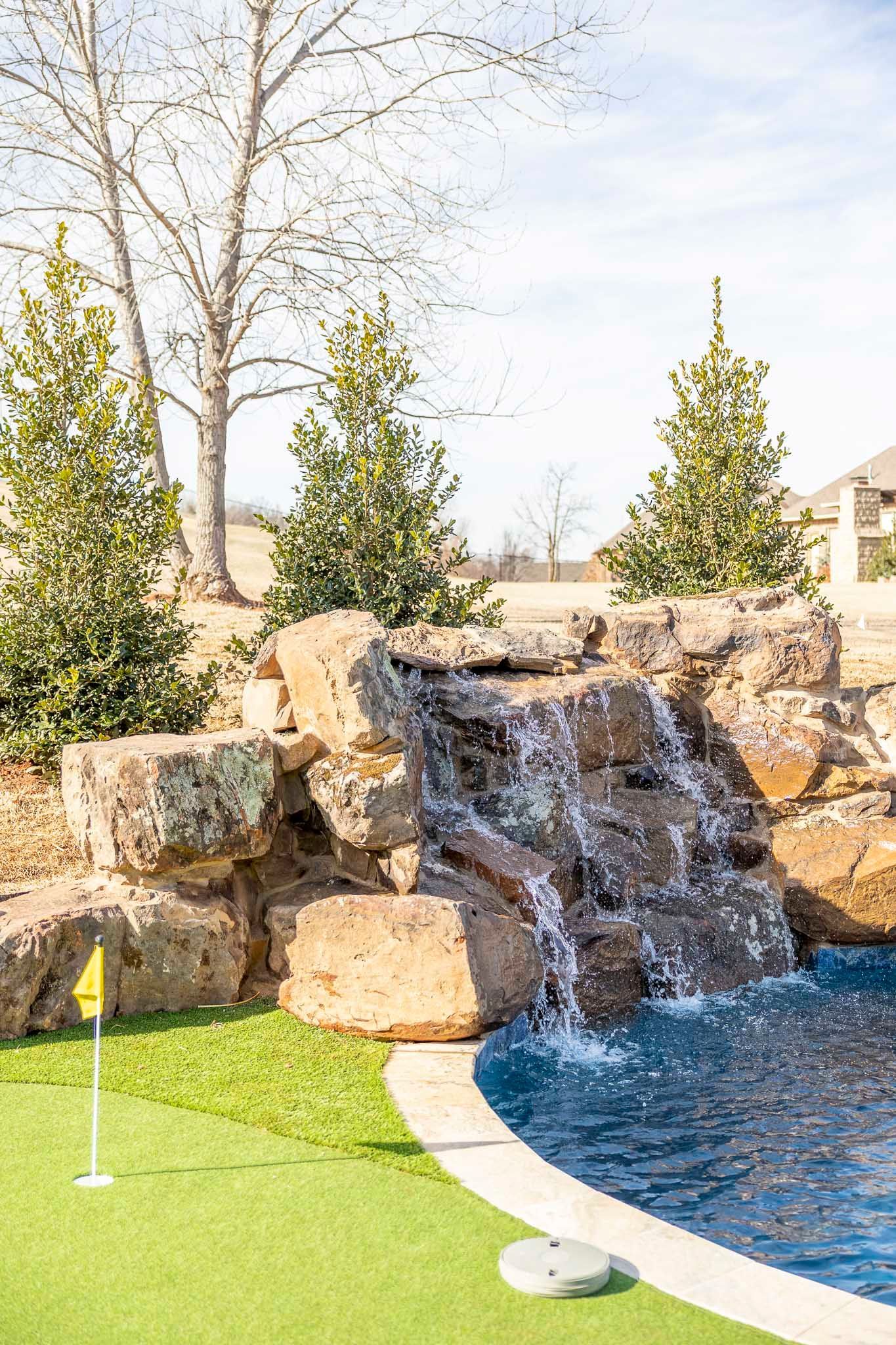There is a waterfall next to a pool and a golf course.