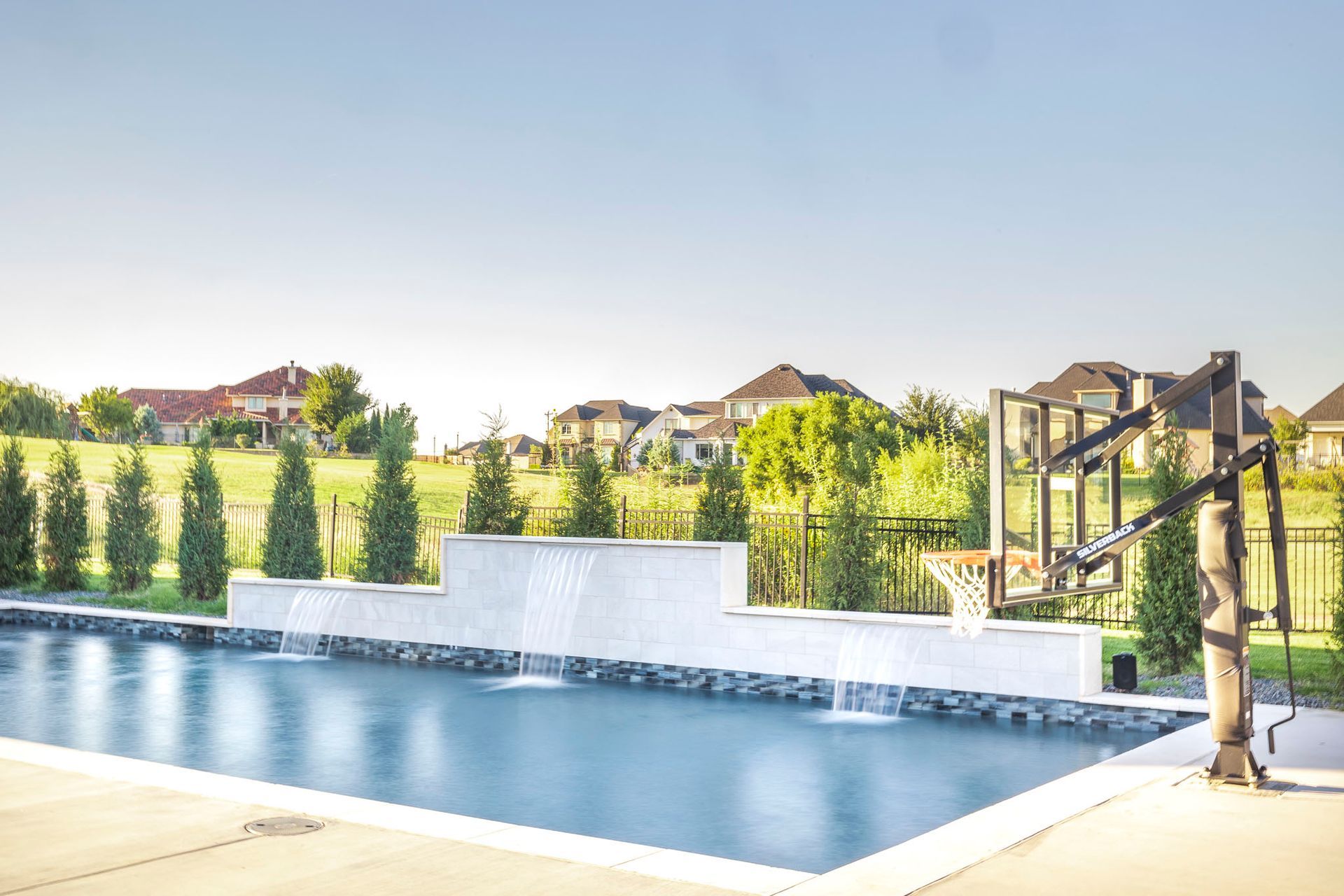 A large swimming pool with a basketball hoop in the backyard of a house.