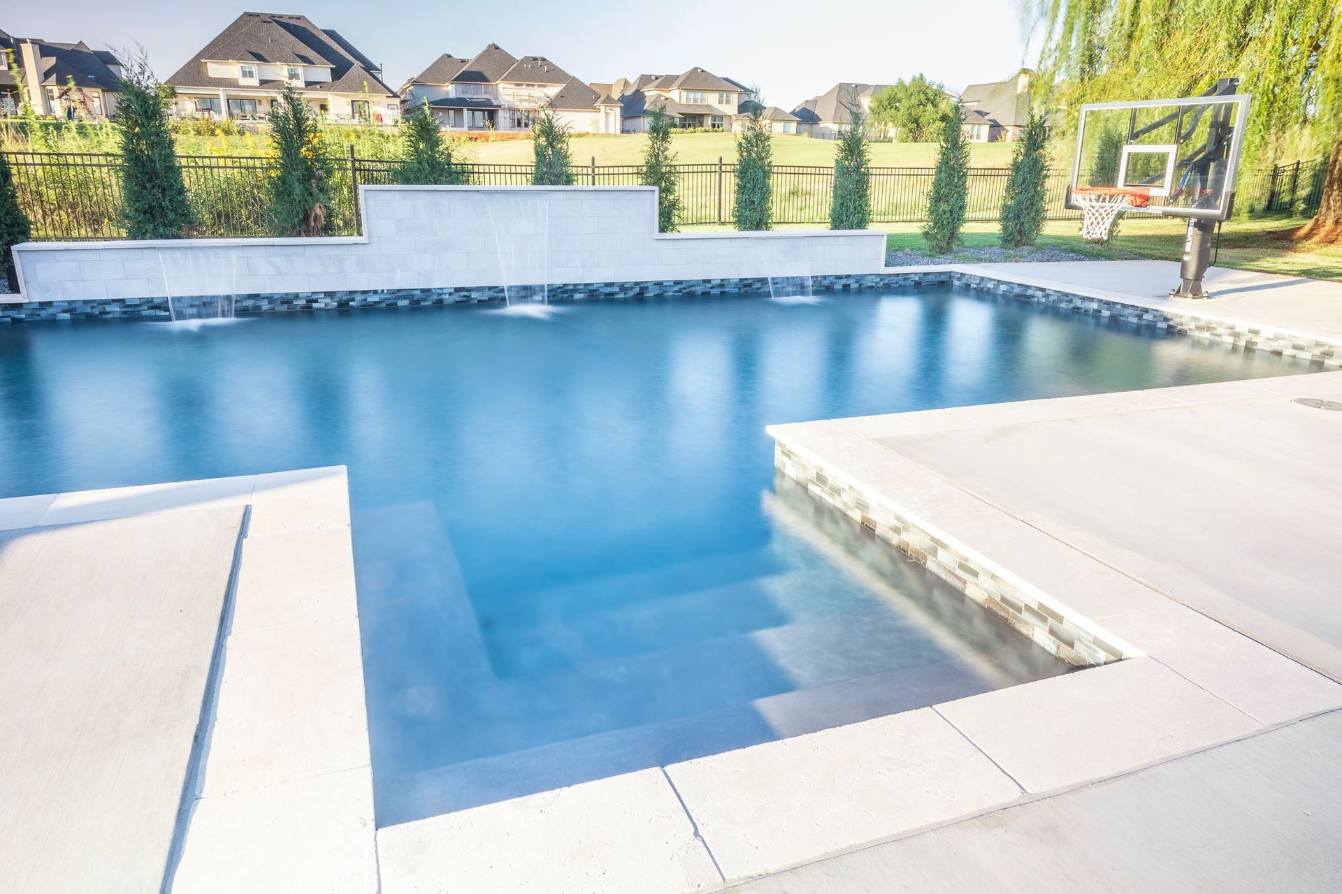 A large swimming pool with a basketball hoop in the backyard.