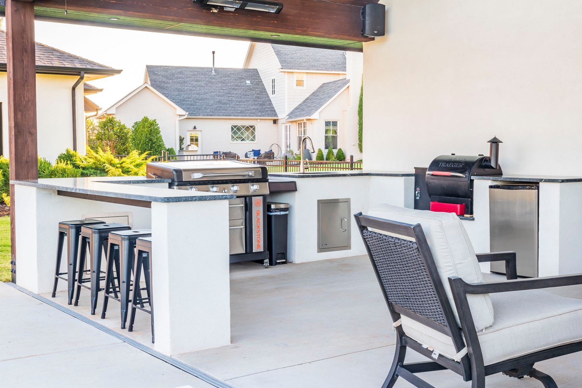 A patio with a table , chairs , stools and a grill.