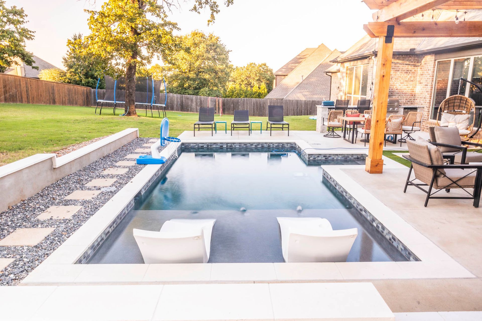 A large swimming pool in a backyard with chairs and a pergola.