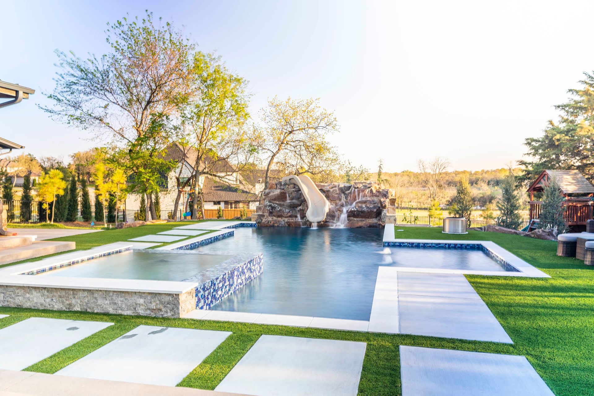 A large swimming pool with a water slide in the backyard of a house.