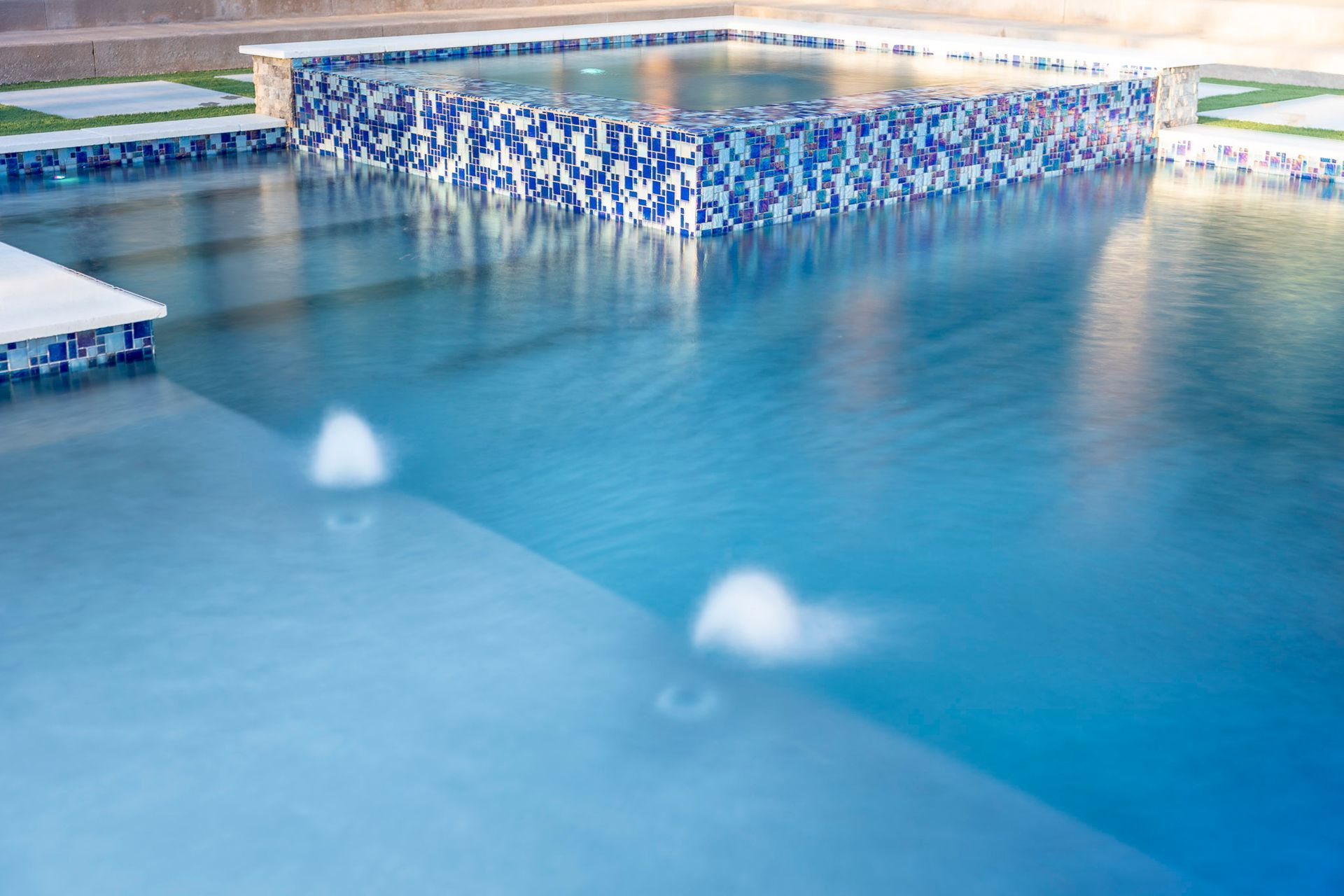 A large swimming pool with blue tiles and a hot tub in the middle.