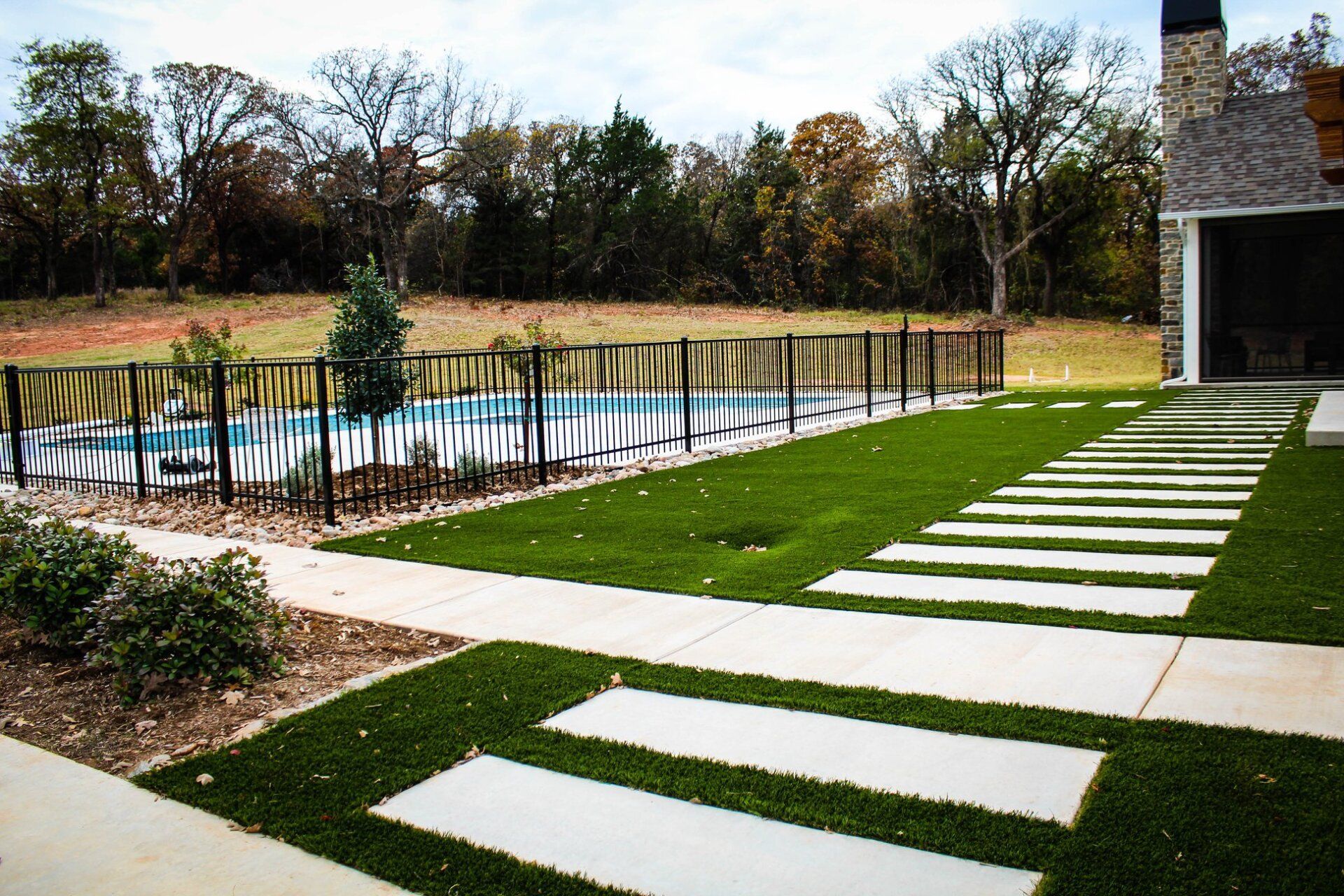 A large lawn with a swimming pool in the background and a walkway leading to it.