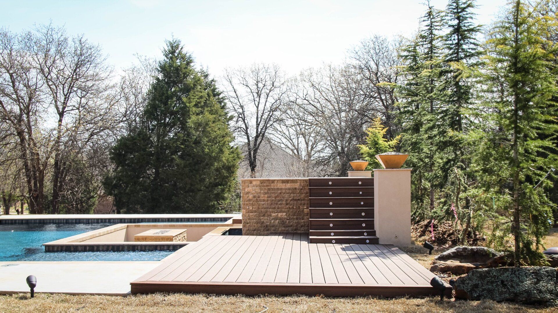 A wooden deck next to a swimming pool with trees in the background