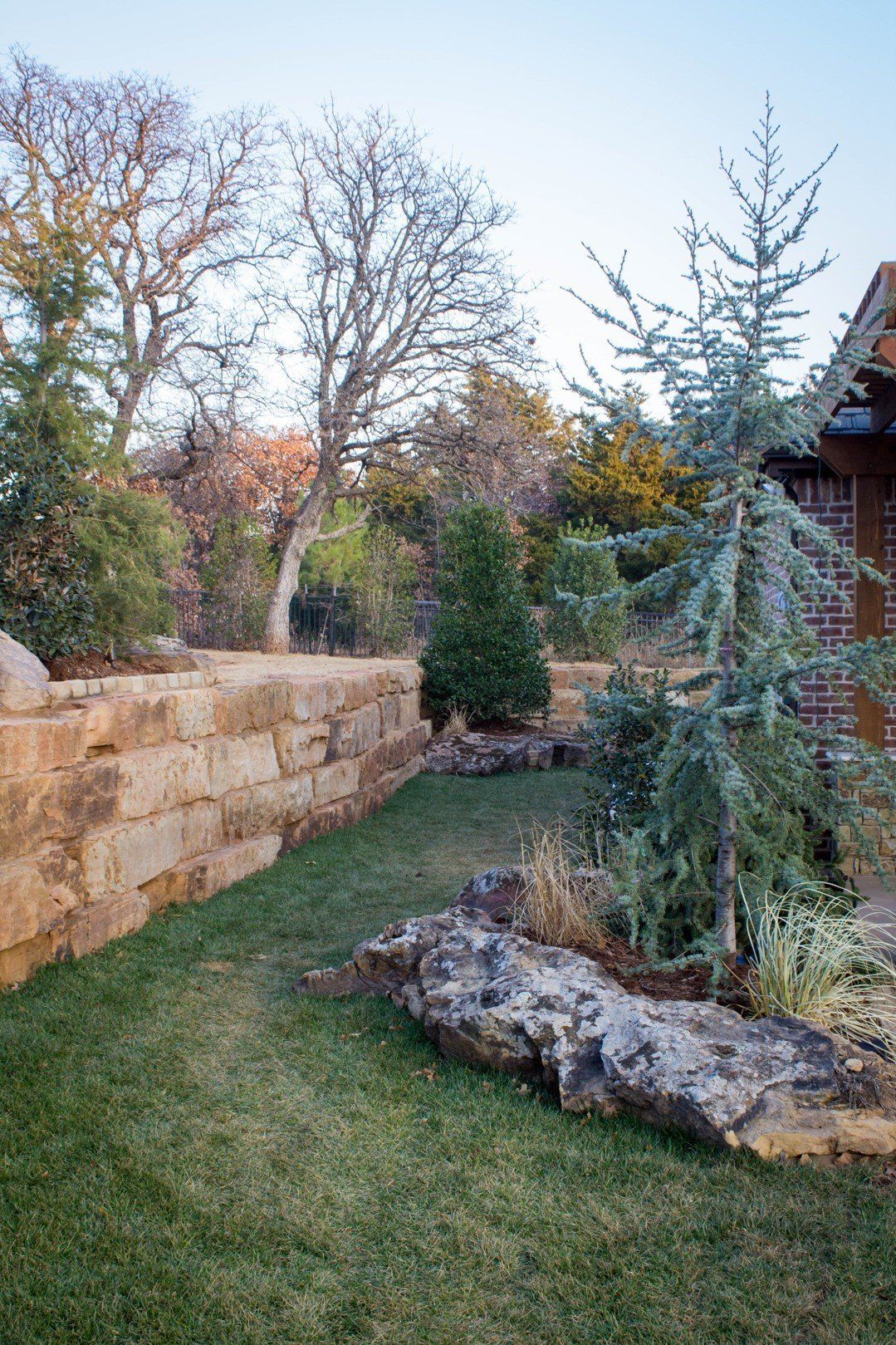 A lush green yard with a stone wall and trees in the background.
