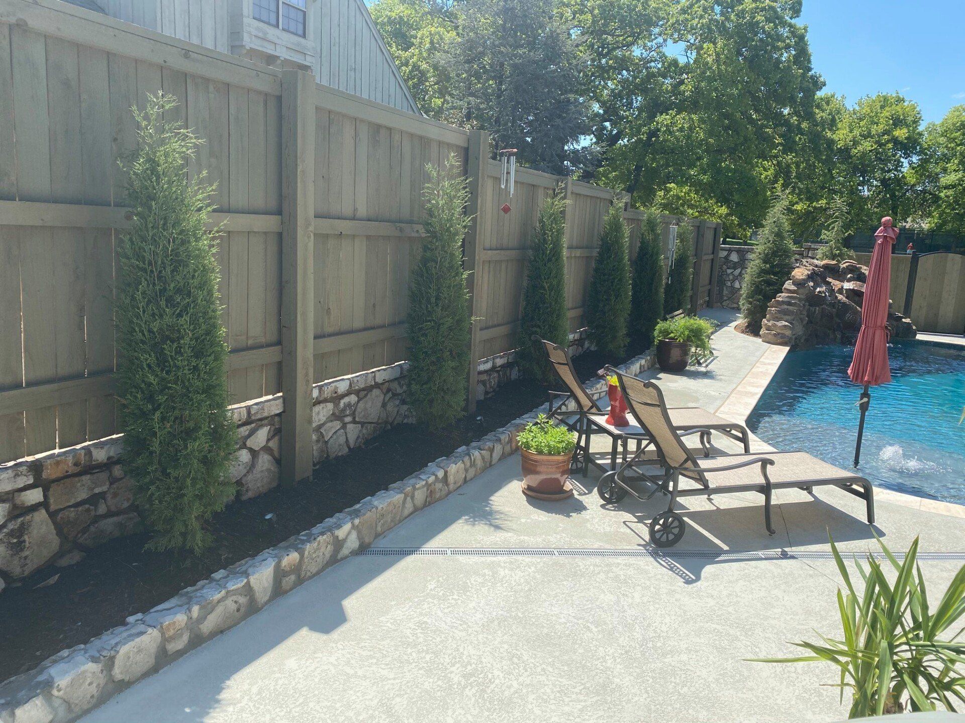 A wooden fence surrounds a swimming pool with chairs and umbrellas.