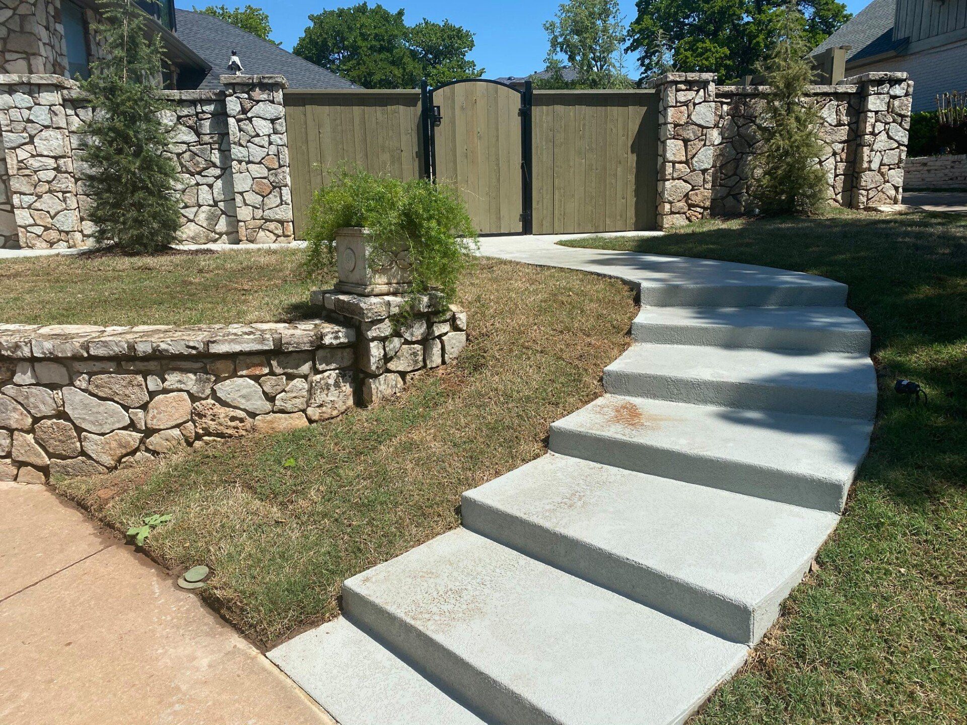A concrete walkway leading to a stone wall and a wooden gate.