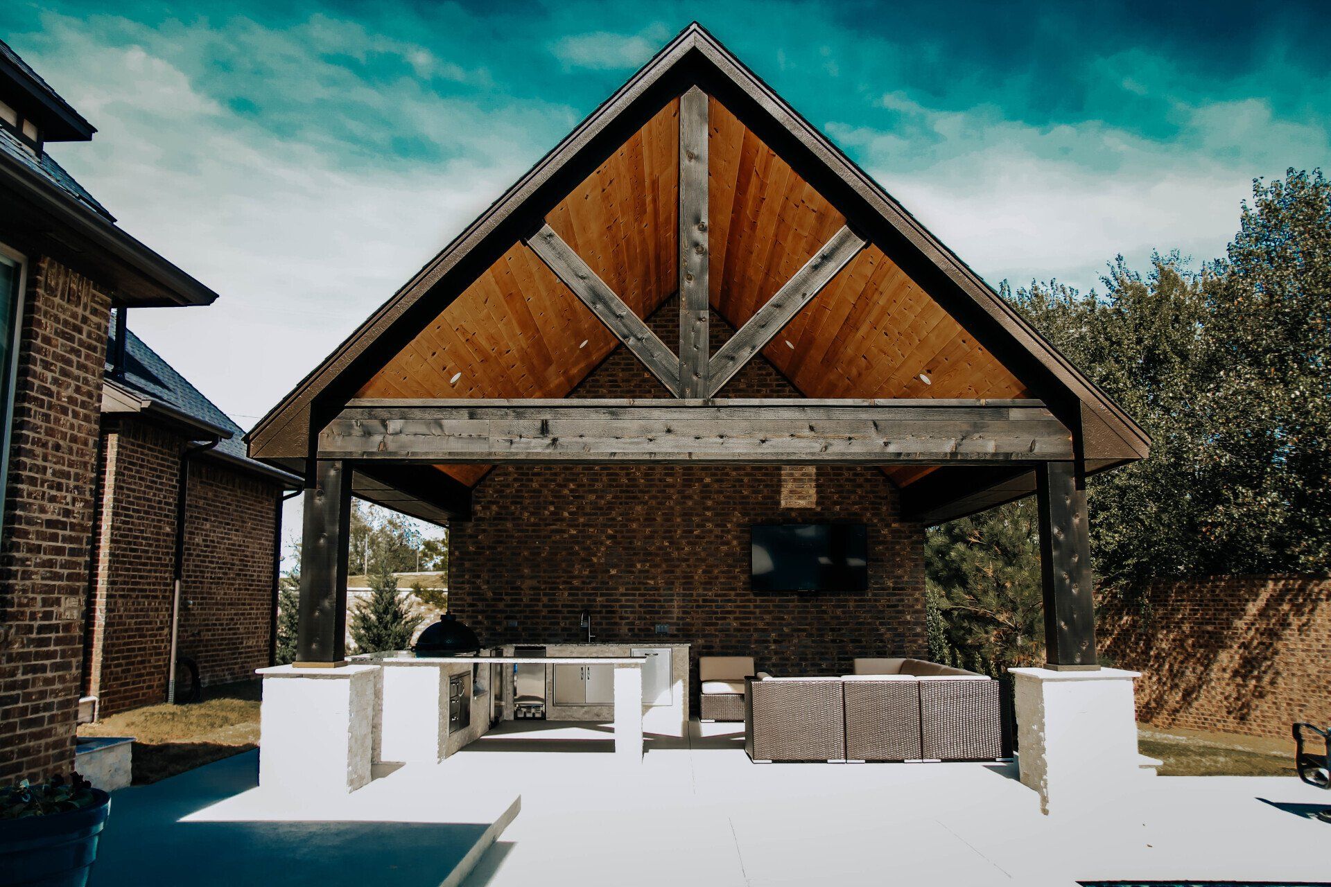 A large covered patio area with a wooden roof and a brick building in the background.