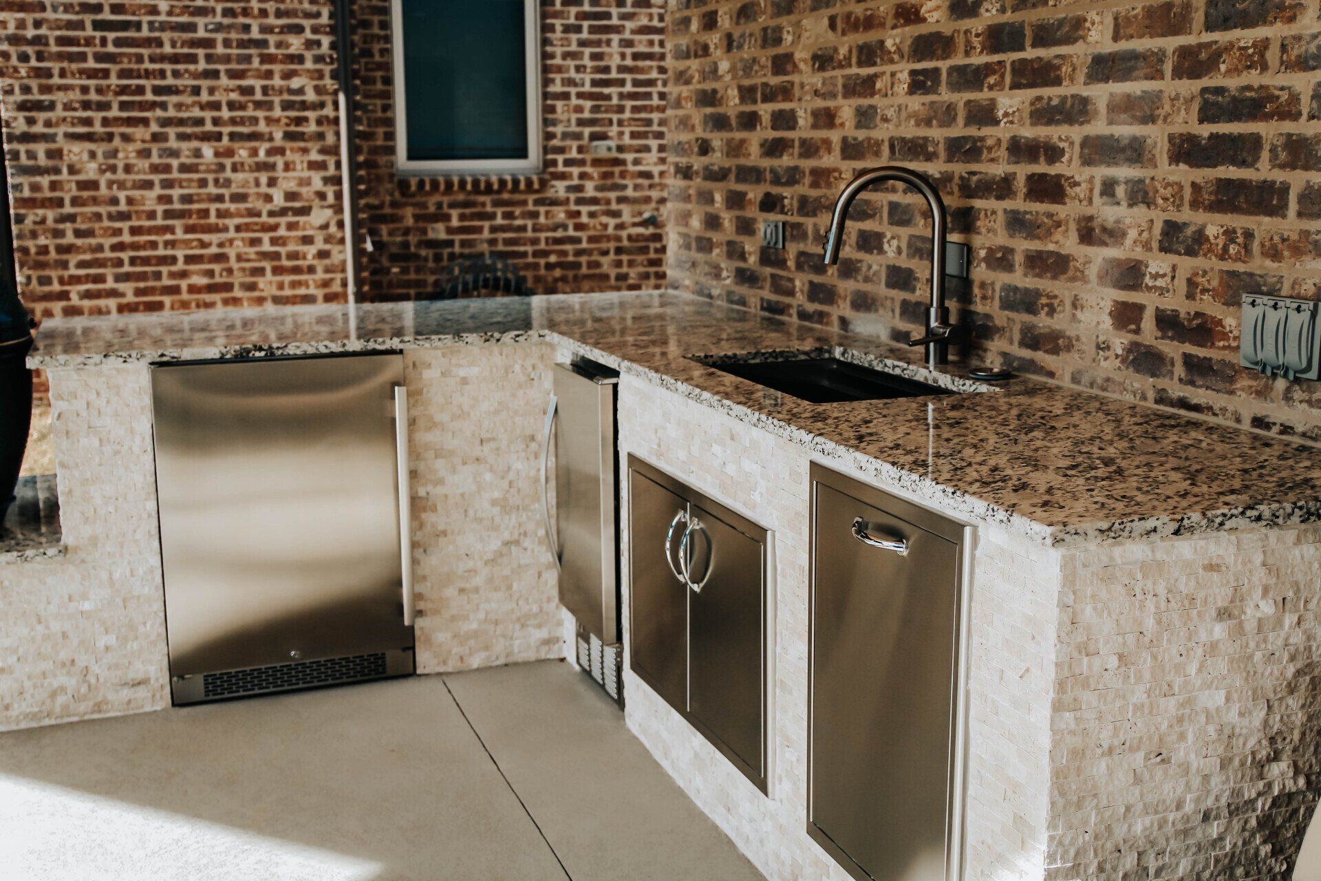A kitchen with granite counter tops , stainless steel appliances , and a brick wall.