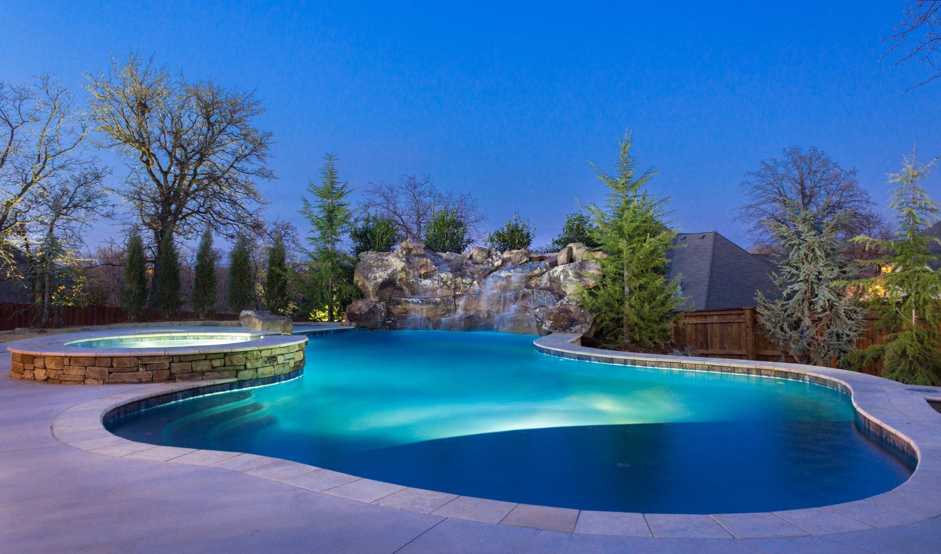 A large swimming pool with a waterfall in the backyard at night.