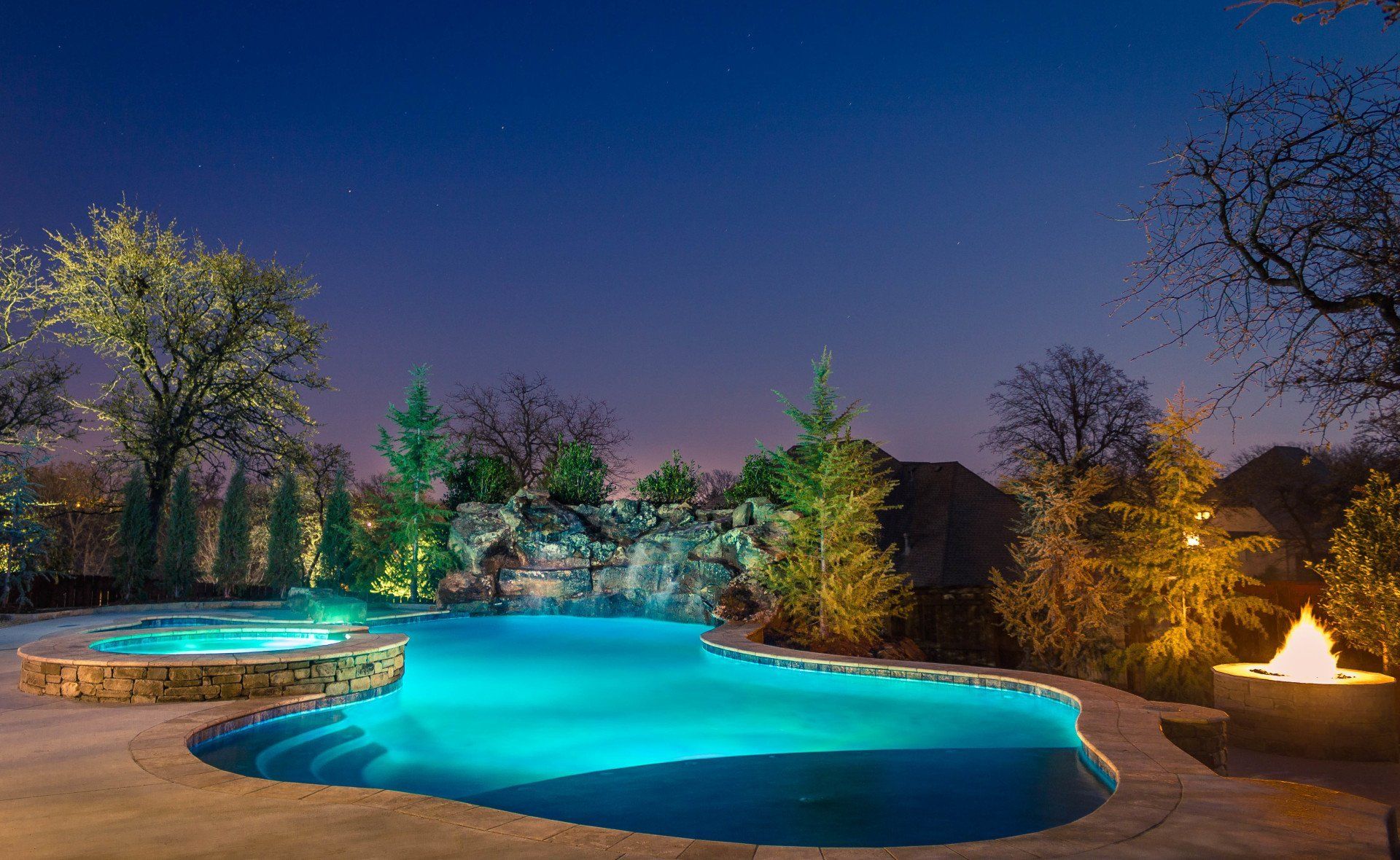 A large swimming pool is lit up at night with trees in the background.
