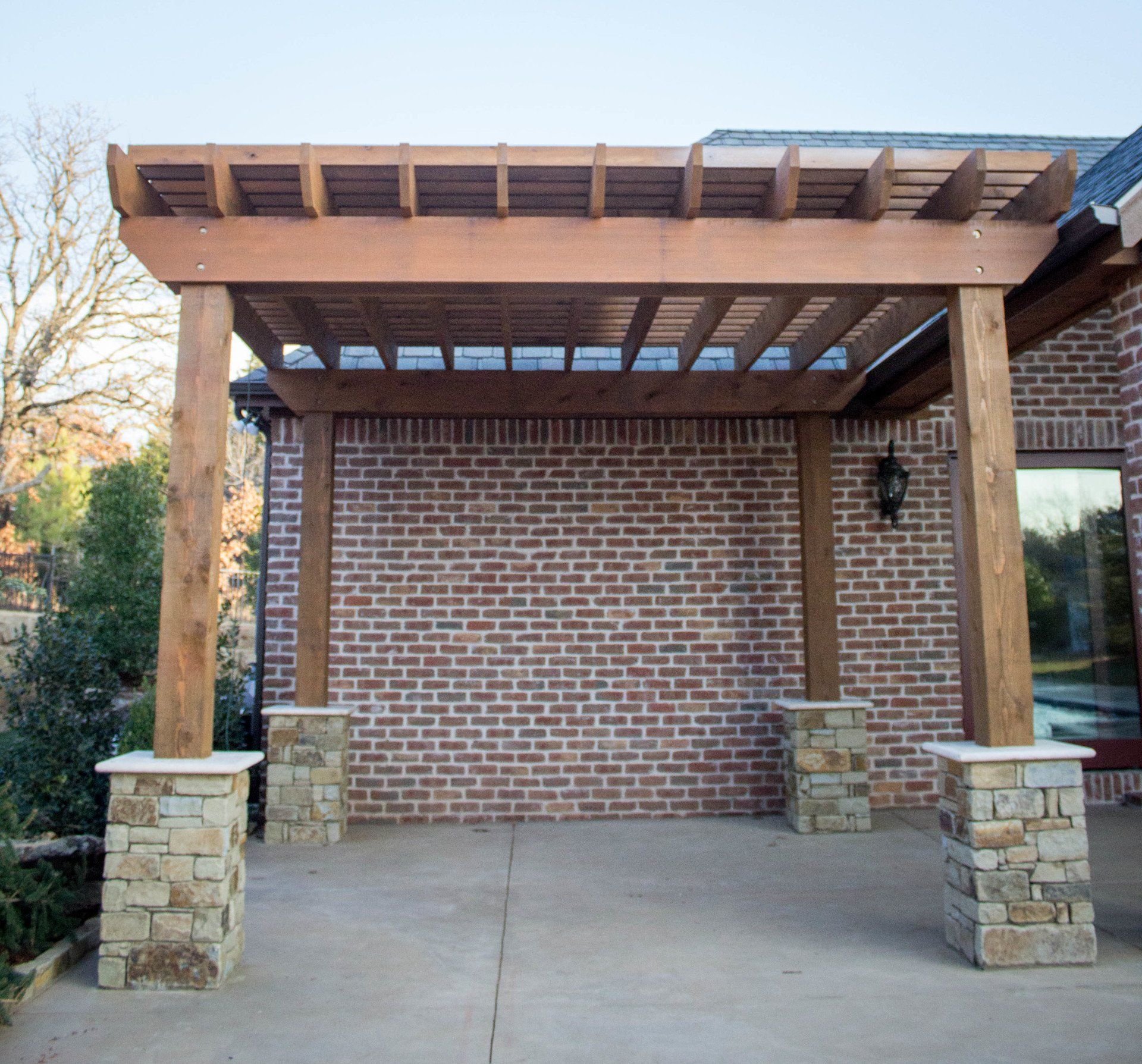 A wooden pergola is in front of a brick building
