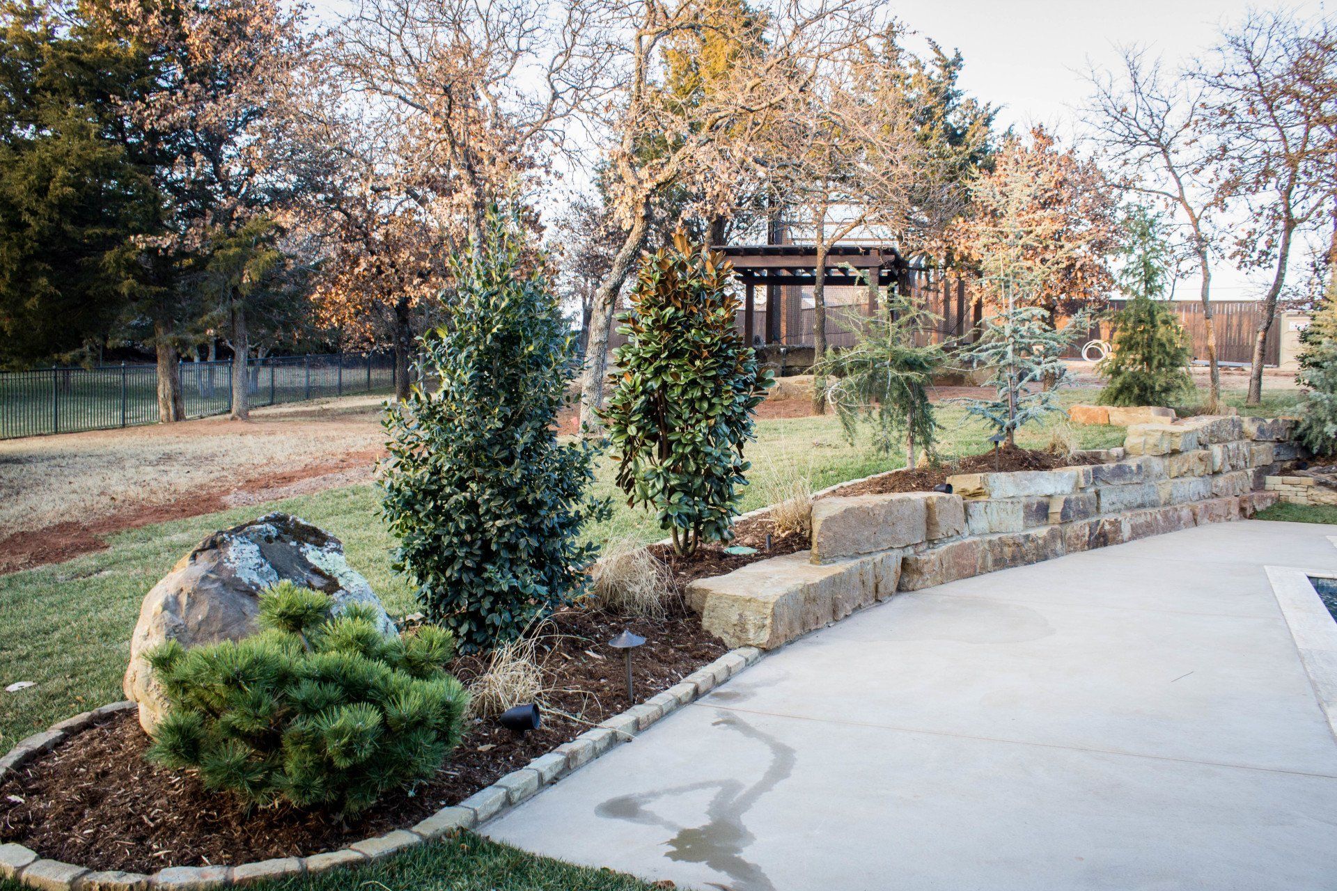 A concrete walkway leading to a house surrounded by trees and bushes.
