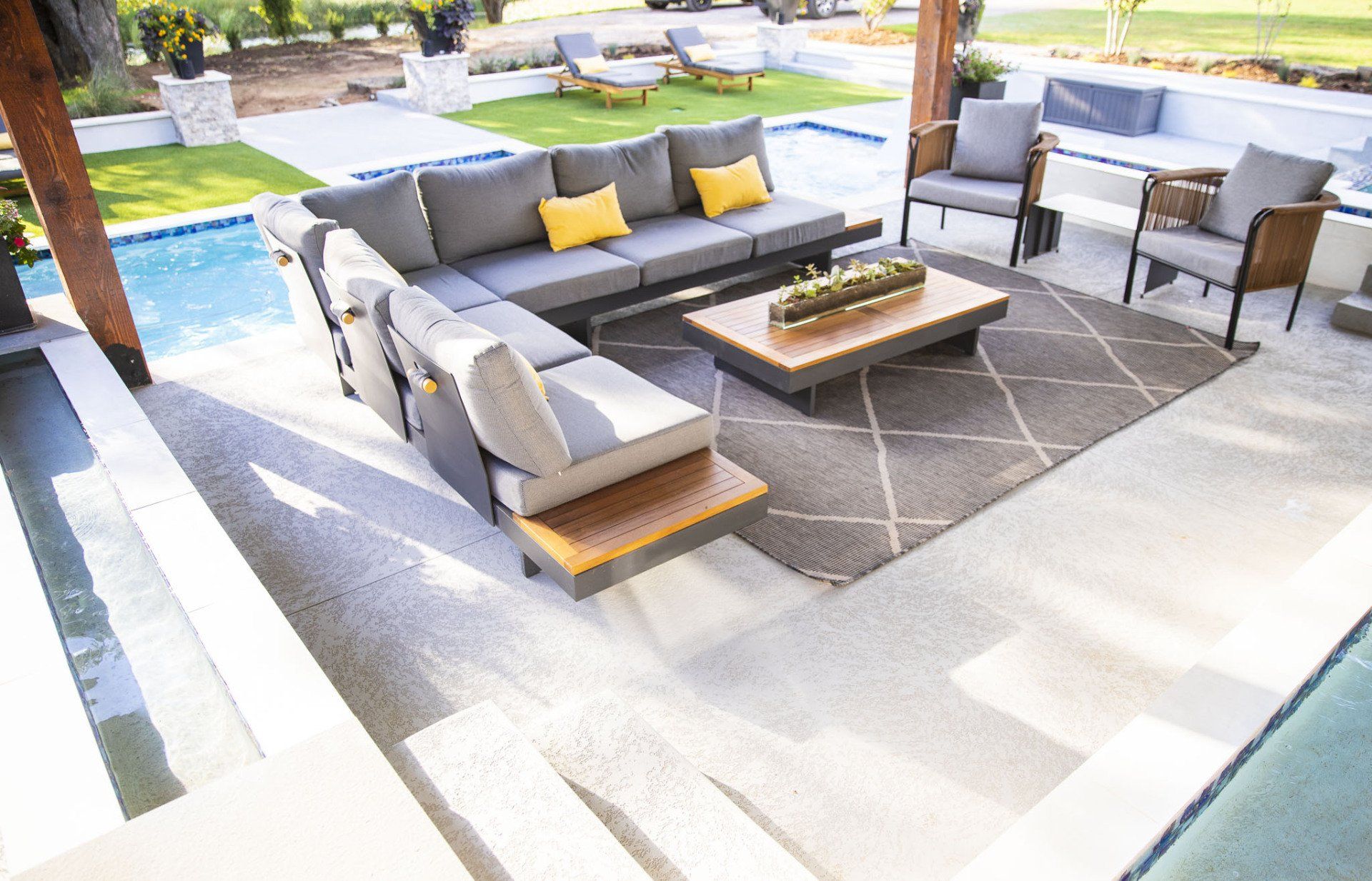 A patio with a couch , chairs , and a coffee table next to a pool.