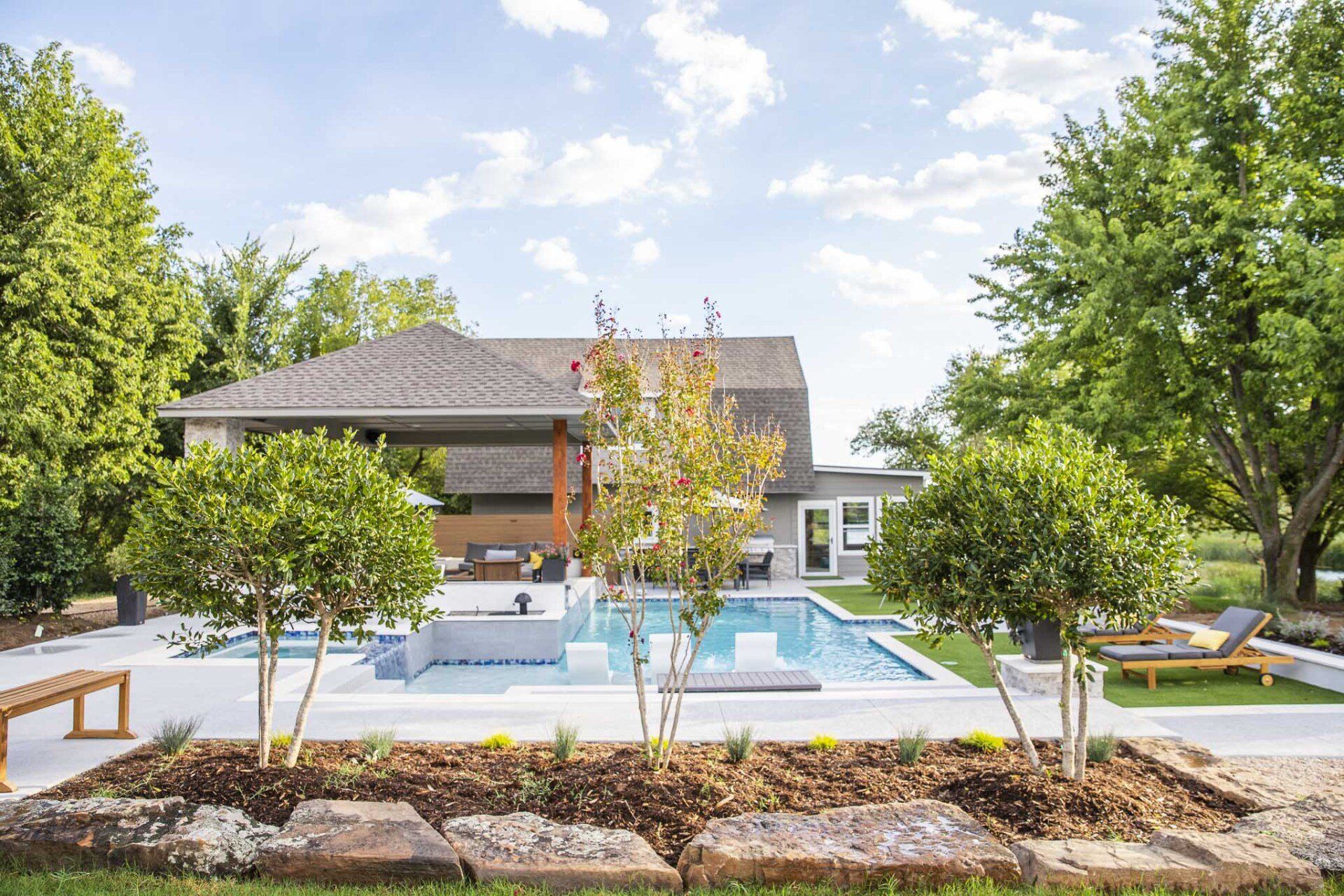 A large swimming pool is in the backyard of a house surrounded by trees.