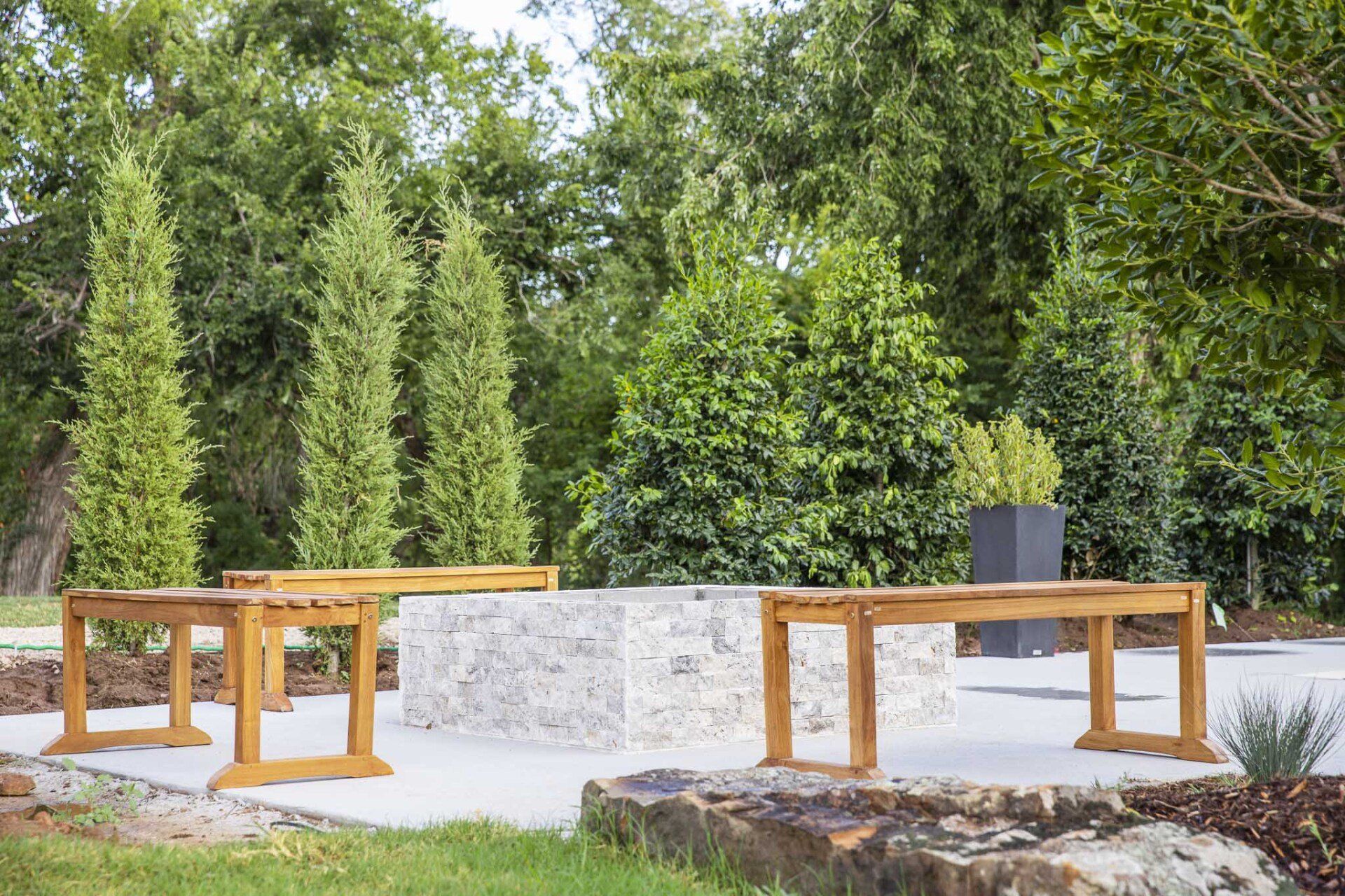 A group of wooden benches sitting around a fire pit in a park.