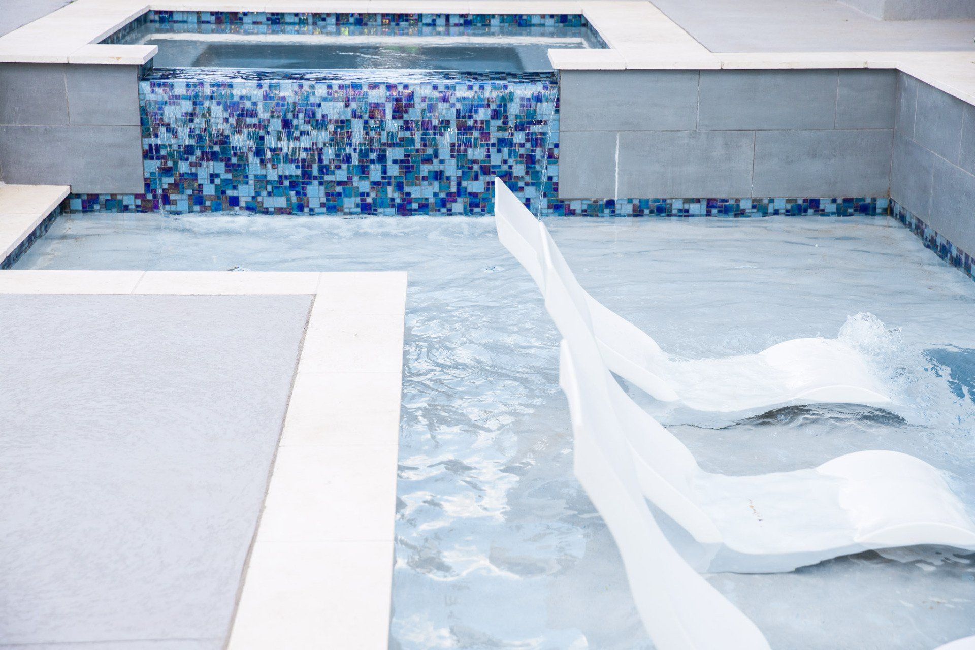 A swimming pool with a waterfall and chairs in it.