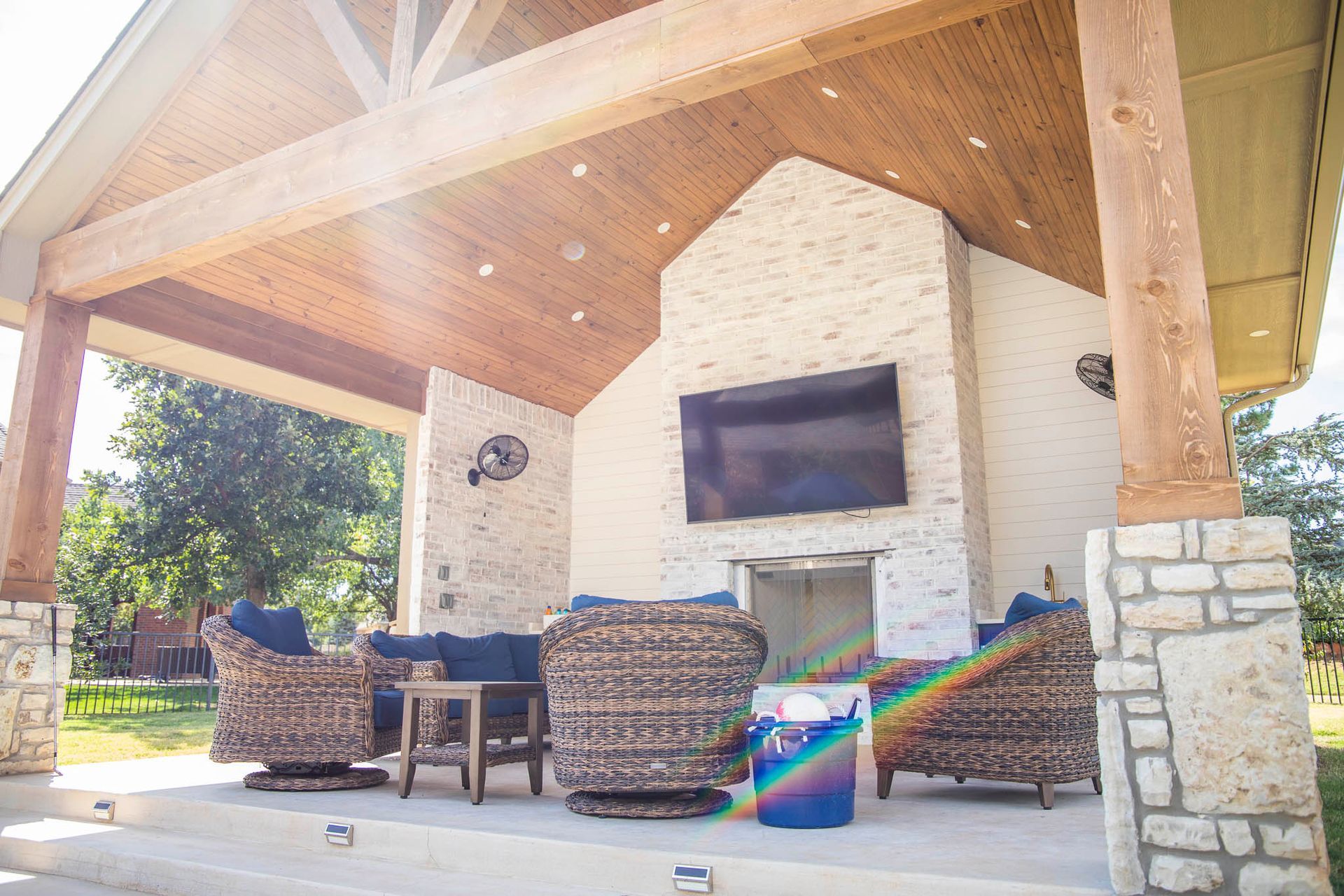 A covered patio with a fireplace , chairs , and a television.
