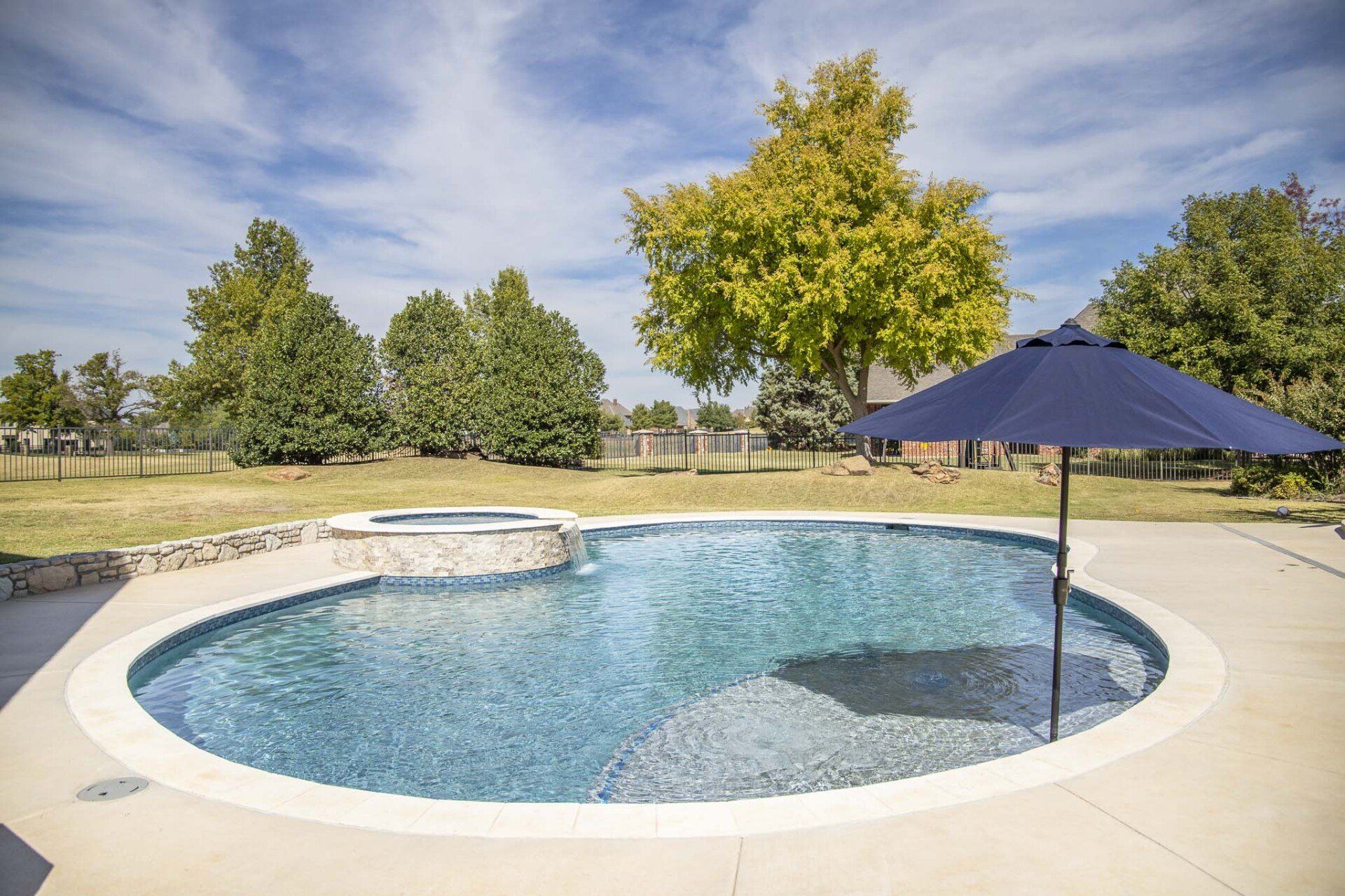 A large swimming pool with a blue umbrella in the middle of it.