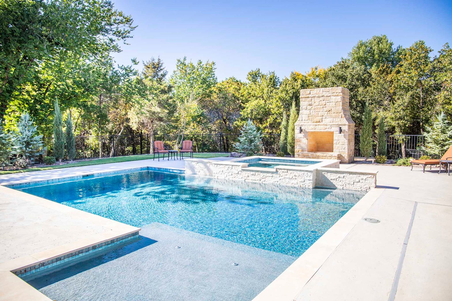 A large swimming pool with a fireplace in the backyard surrounded by trees.