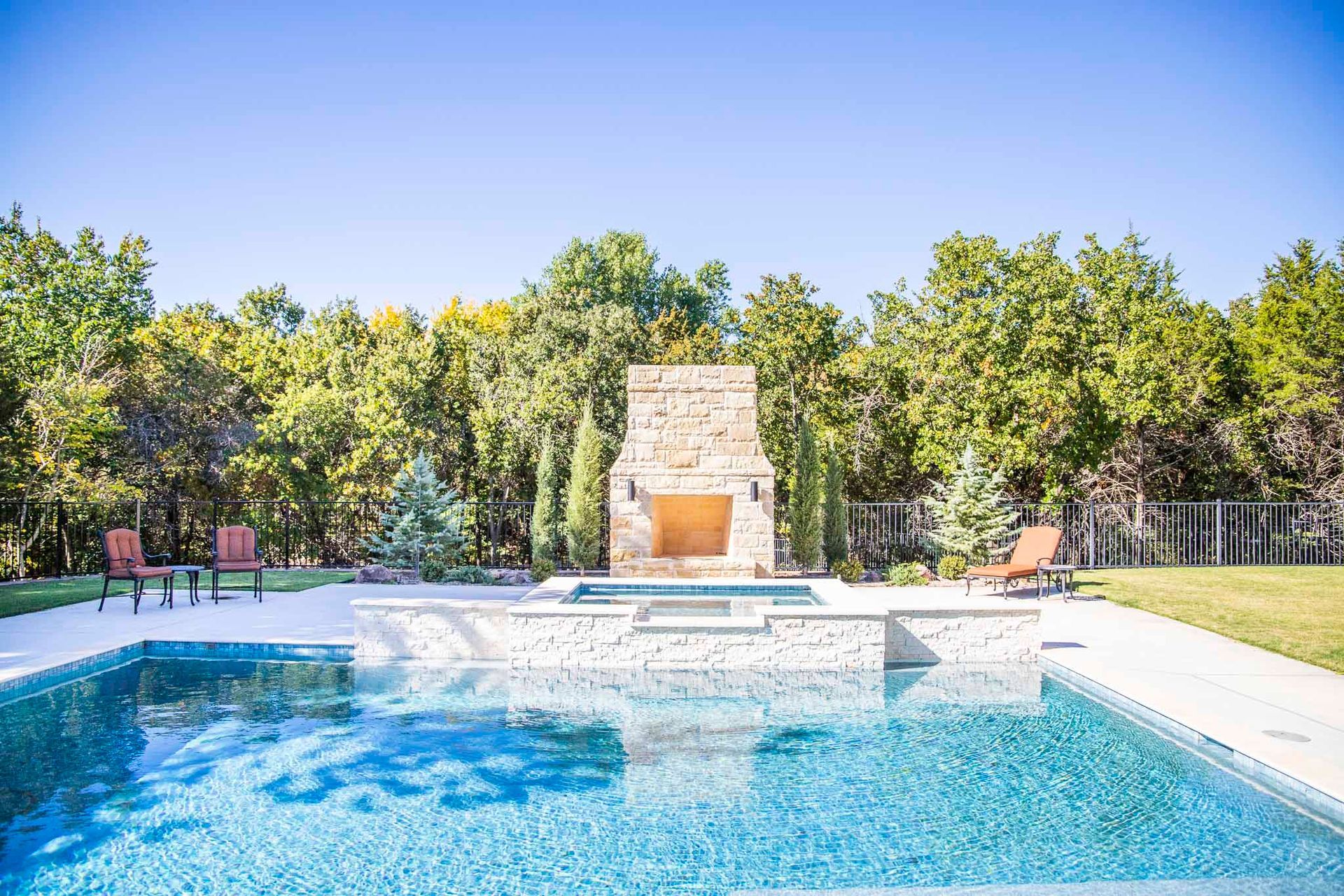 A large swimming pool with a fireplace in the backyard surrounded by trees.