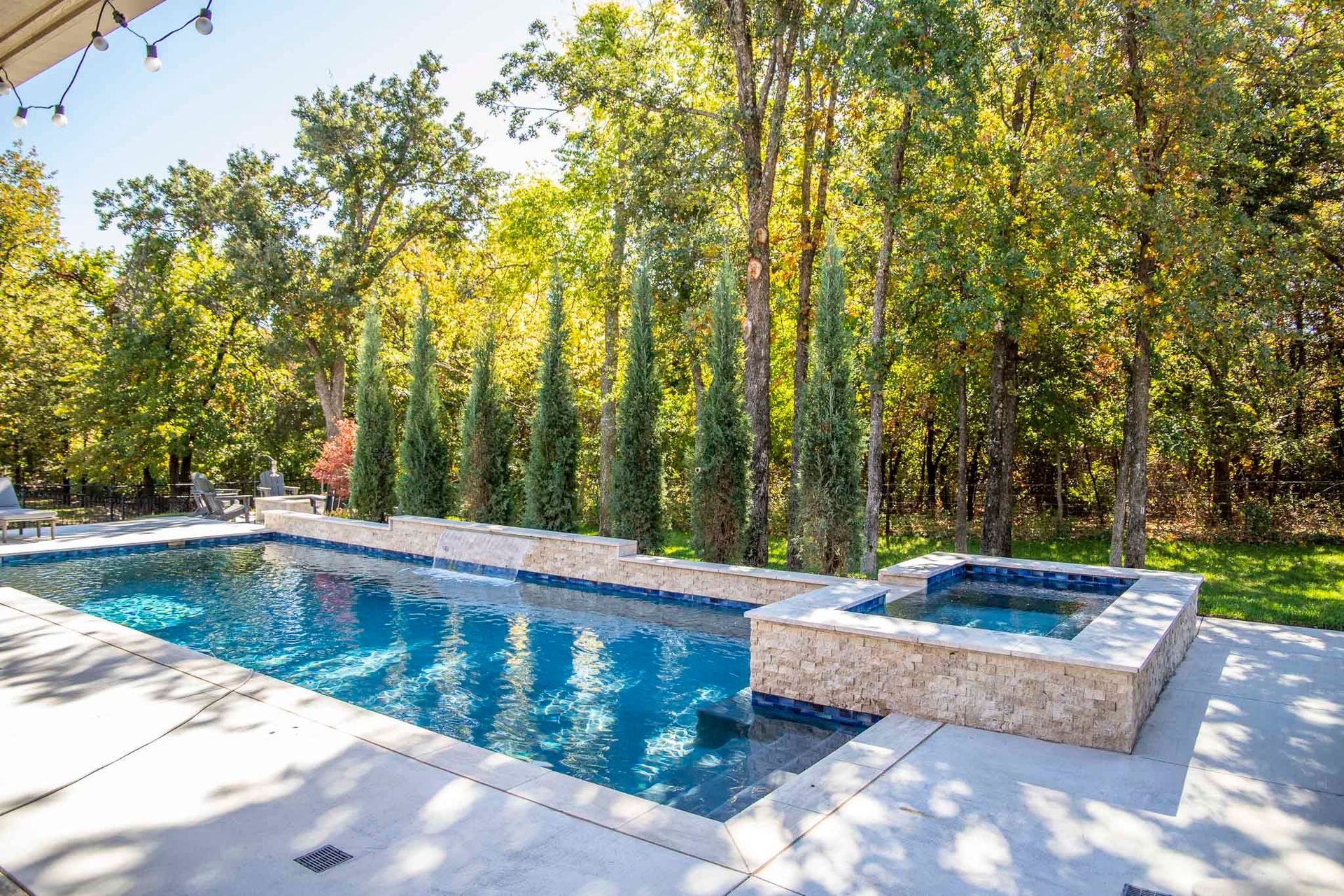 A large swimming pool with a hot tub in the backyard surrounded by trees.