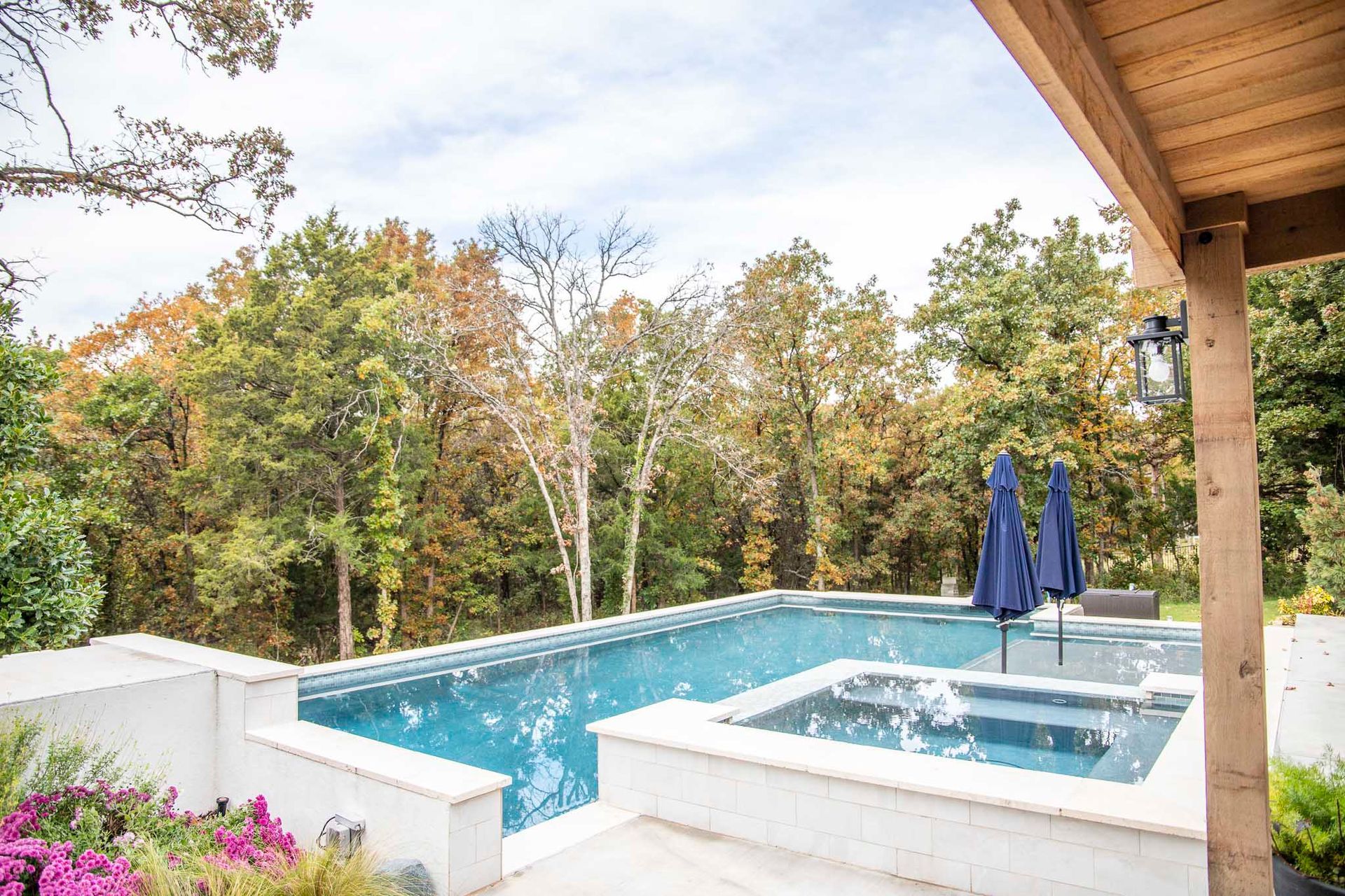 A large swimming pool with umbrellas and a hot tub is surrounded by trees.