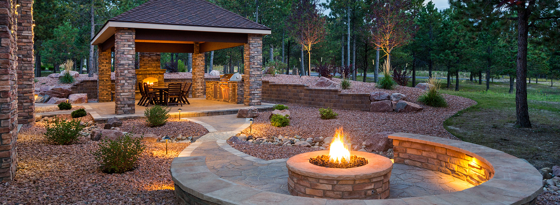 A fire pit in the middle of a yard with a gazebo in the background.