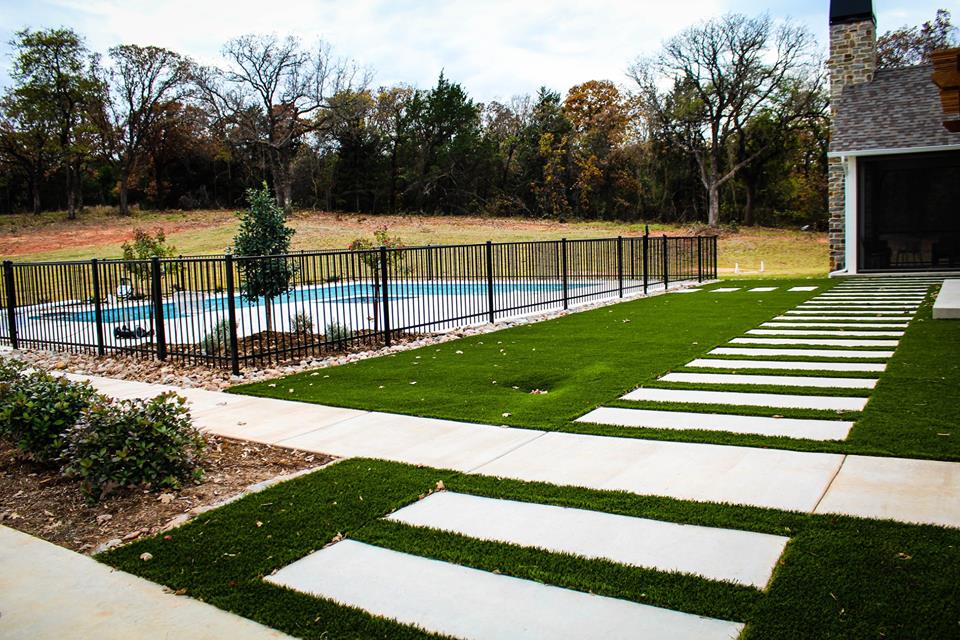 A driveway with a fence and a pool in the background.