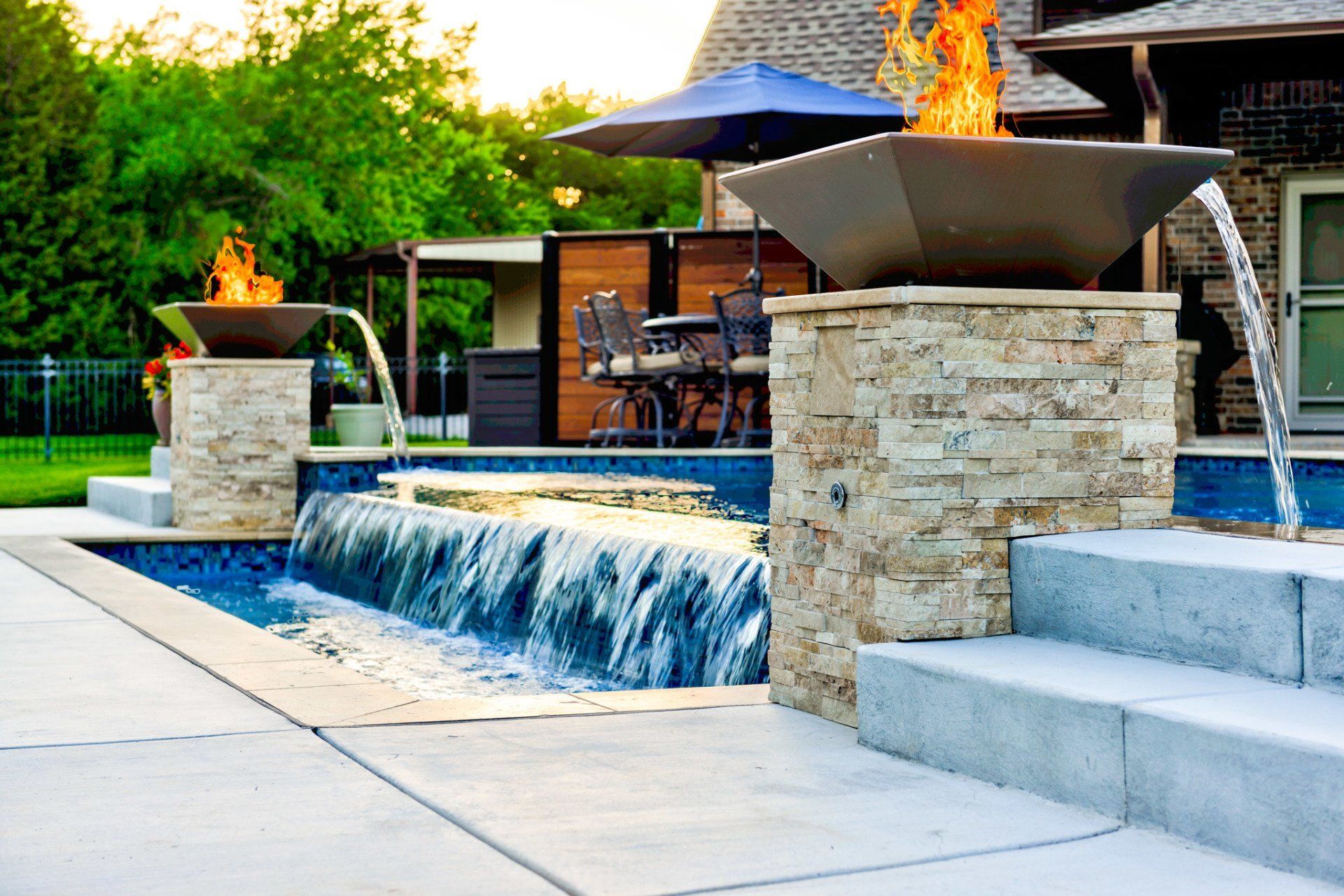 A swimming pool with a waterfall and a fire pit