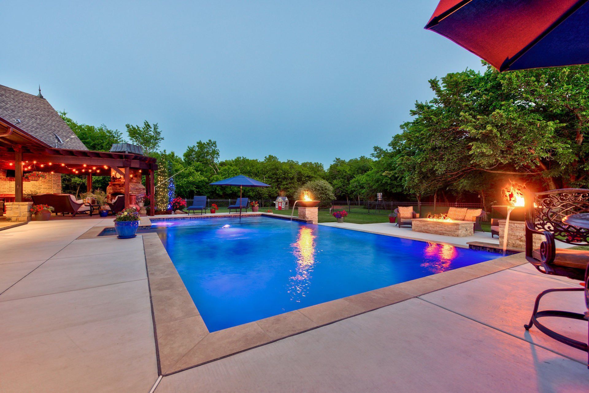 A large swimming pool is lit up at night in a backyard.